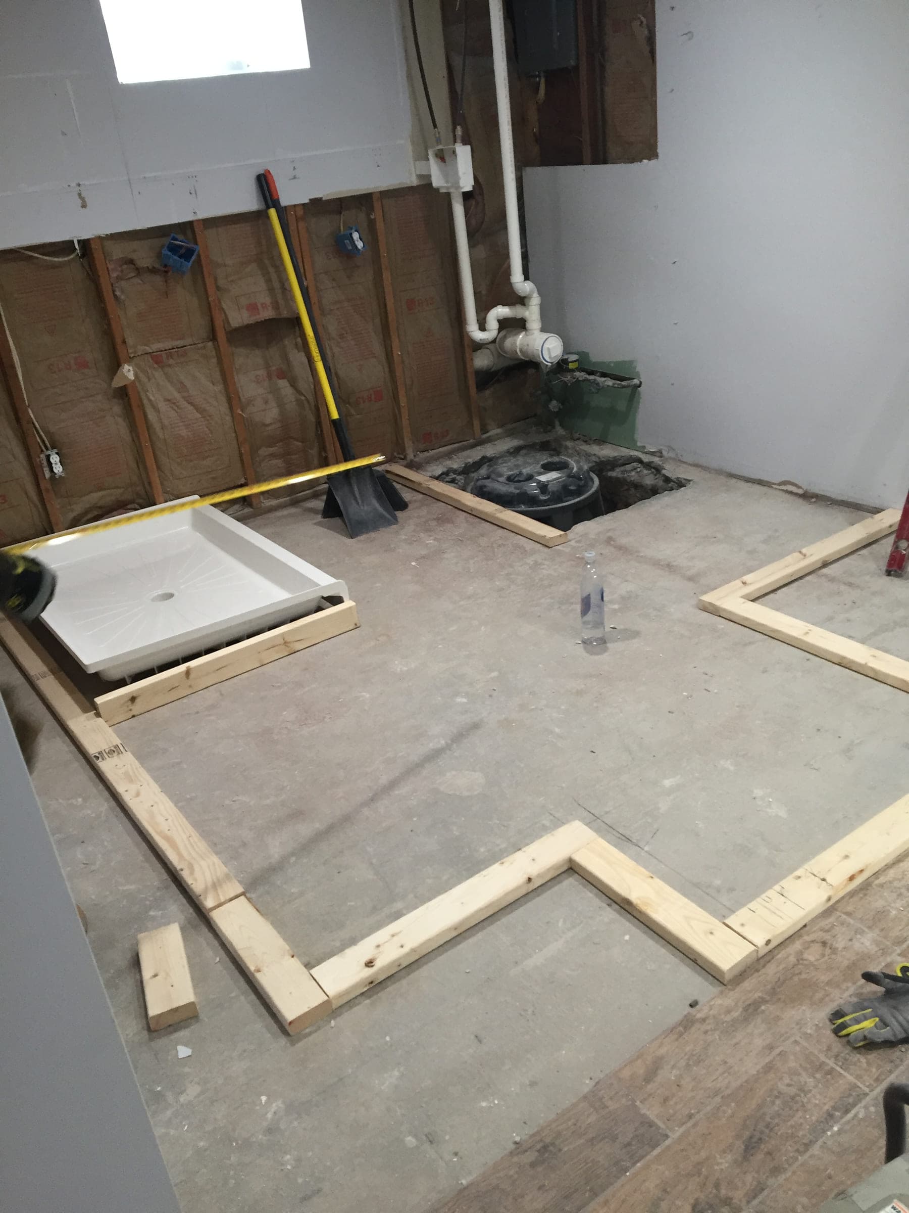 Timber floor plates nailed out across a bare basement slab to mark the new room layout, with a shower tray and an open drain nearby