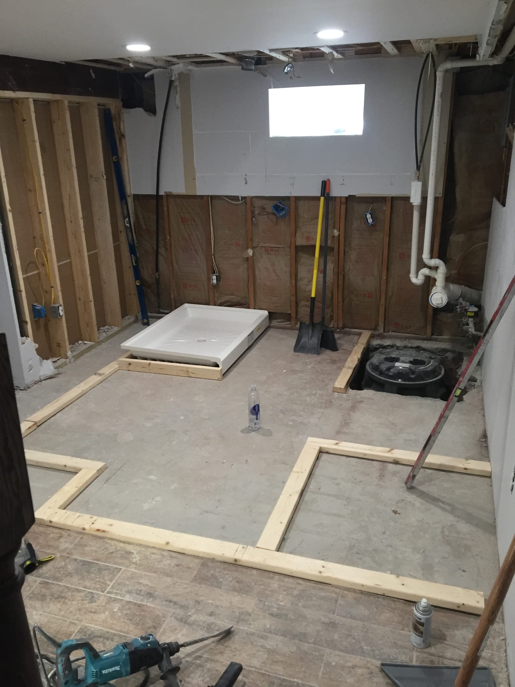 Basement bathroom being framed, with timber floor plates set out on the slab, a shower tray waiting to go in and a waste connection open in the floor