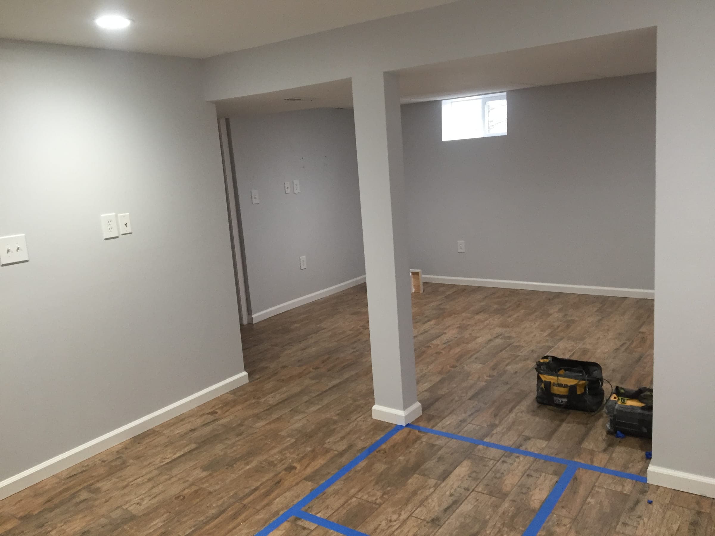 Finished basement showing two boxed columns, an egress window and painted walls above new plank flooring