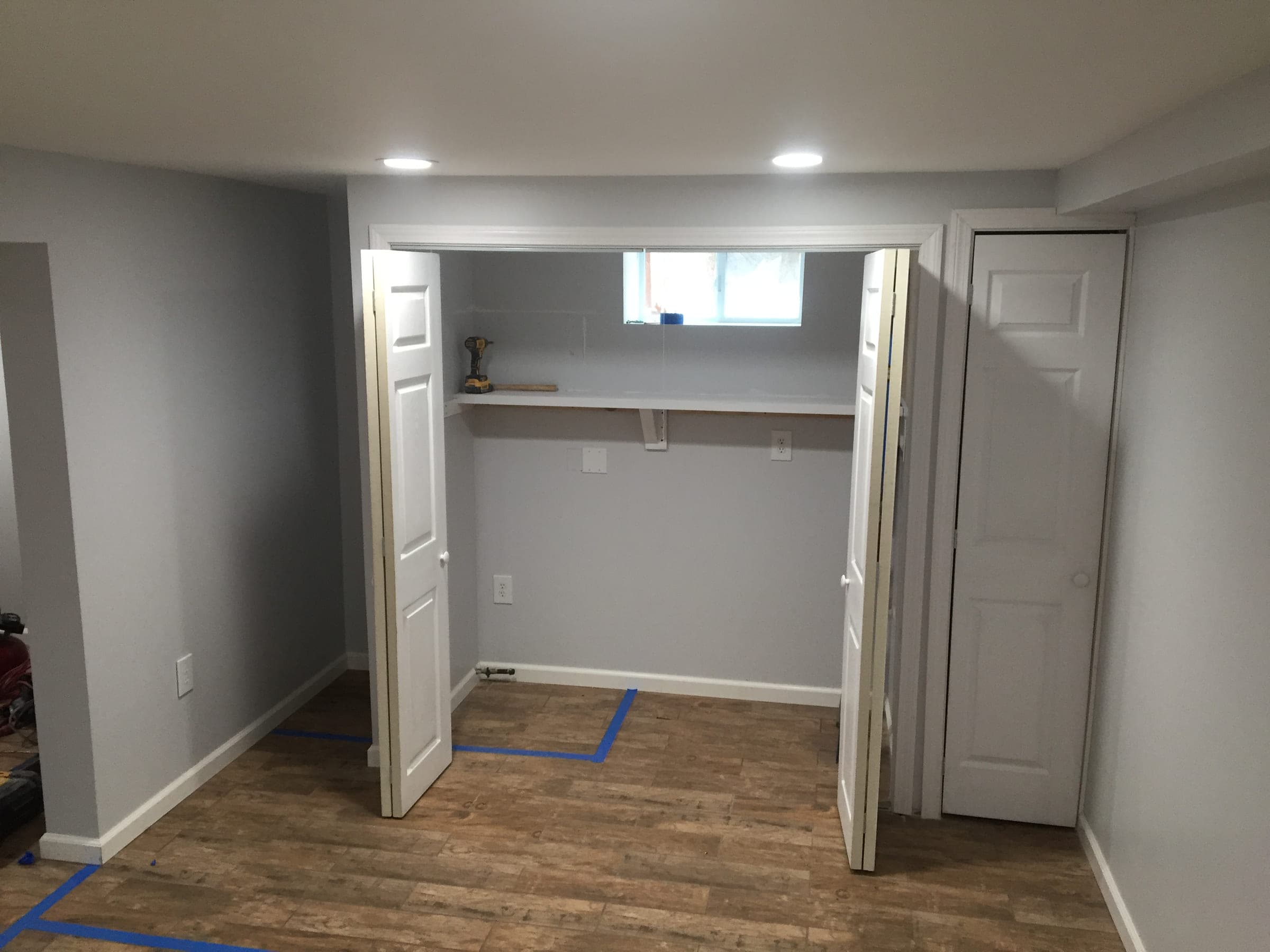 Built-in basement storage closet with a shelf and a window, finished with painted walls and six-panel bifold doors
