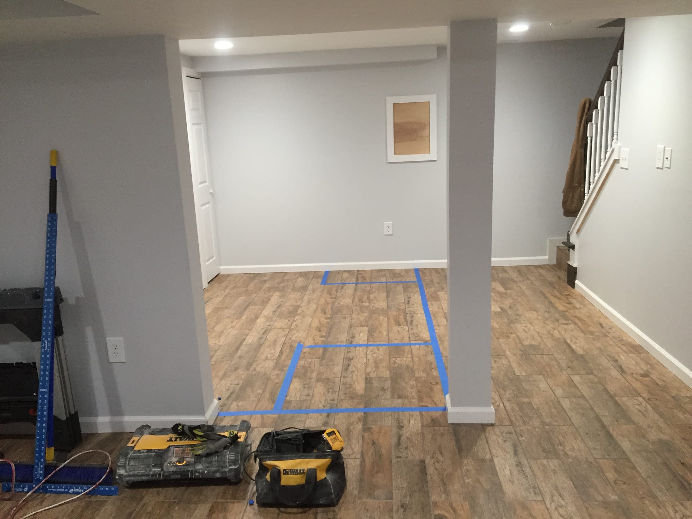 Finished basement living area looking towards the staircase, with a boxed structural column, painted walls and wood-effect plank flooring