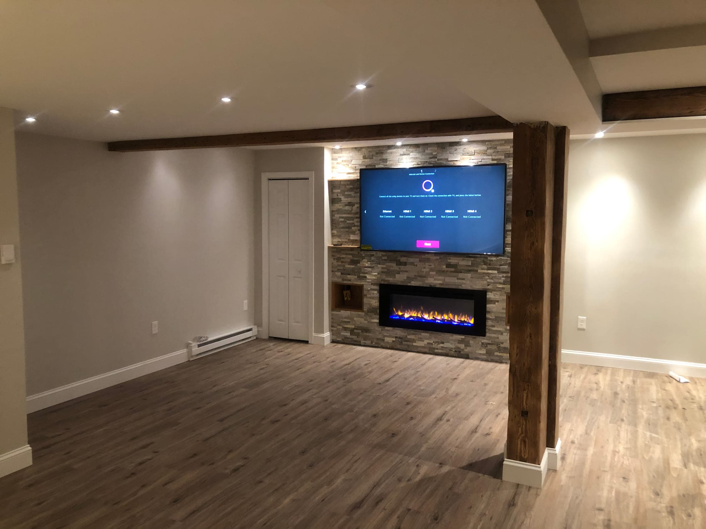 Finished basement living space with a stacked stone fireplace wall, timber beams, recessed lighting and wood-effect flooring