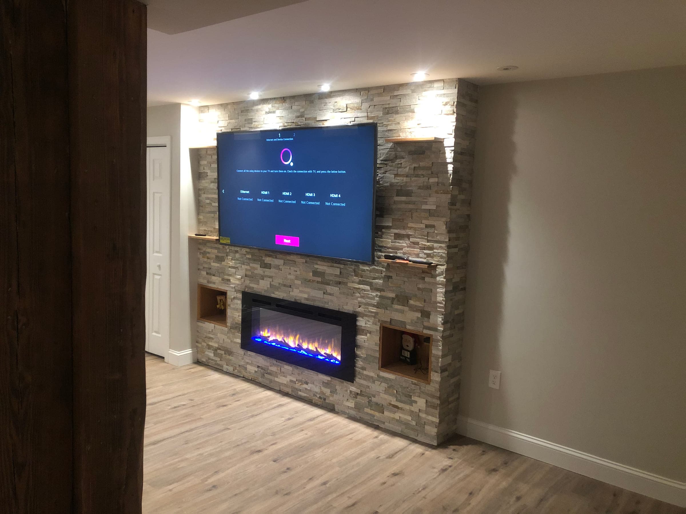 Stacked stone fireplace wall with a linear fire, recessed niches and a reclaimed timber post in a finished basement