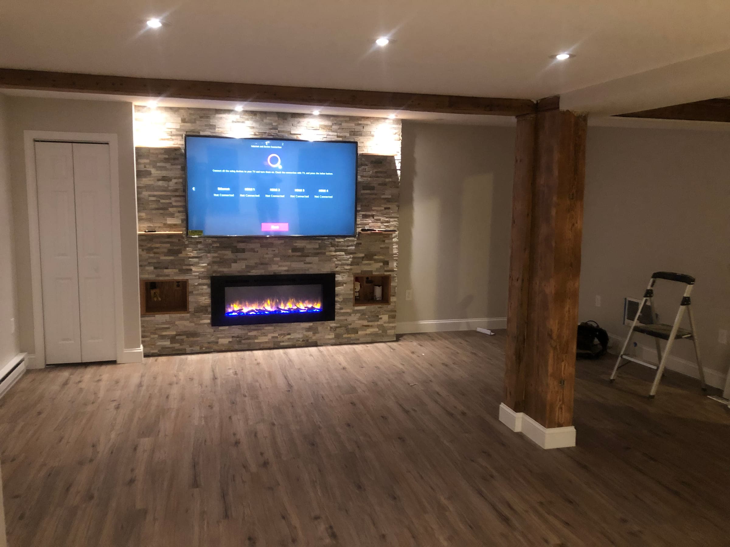 Stacked stone feature wall with a linear electric fireplace and a wall-mounted television in a finished basement