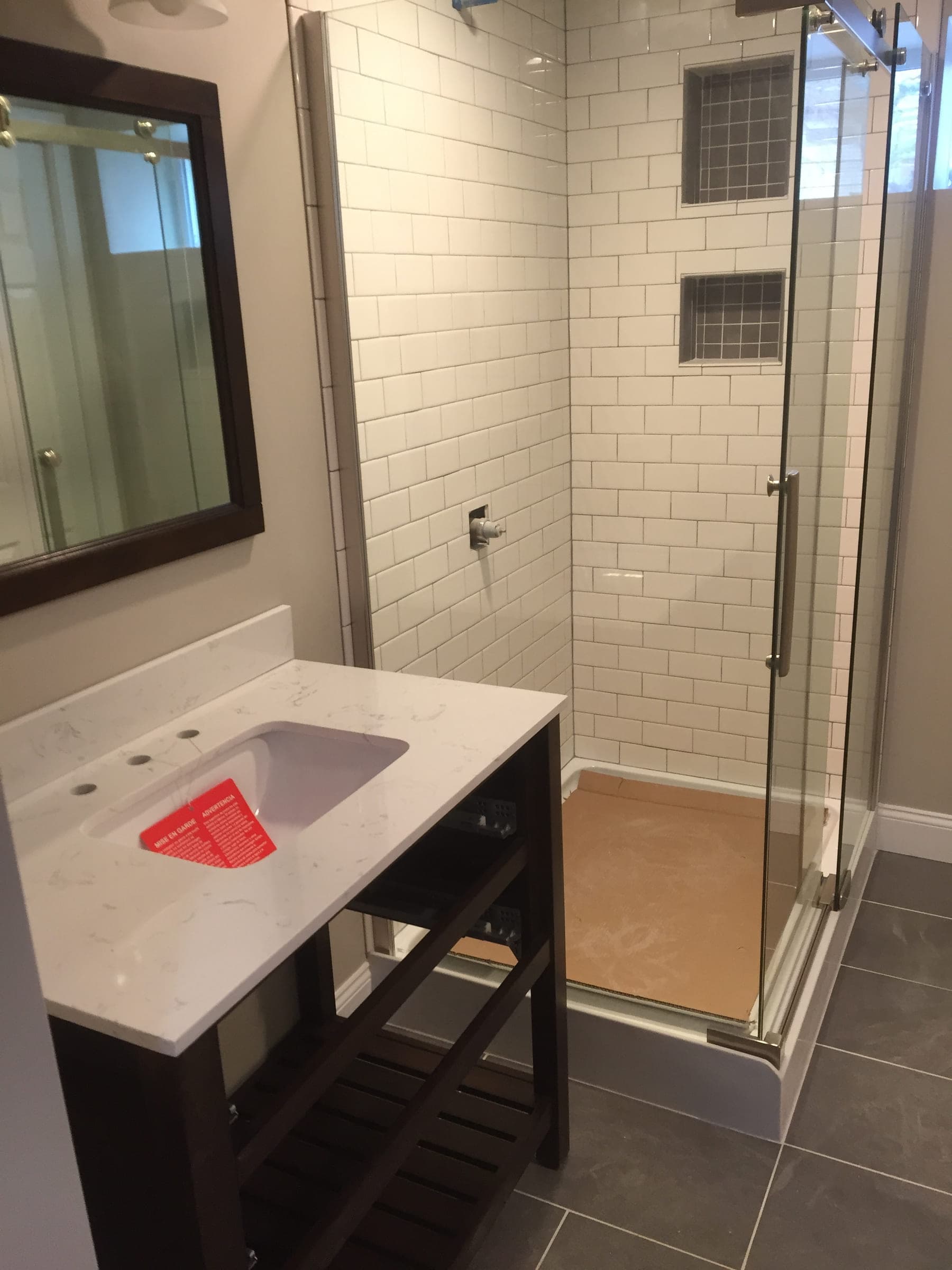 Bathroom with a subway tiled shower behind a glass enclosure, a dark vanity with a stone top and a framed mirror