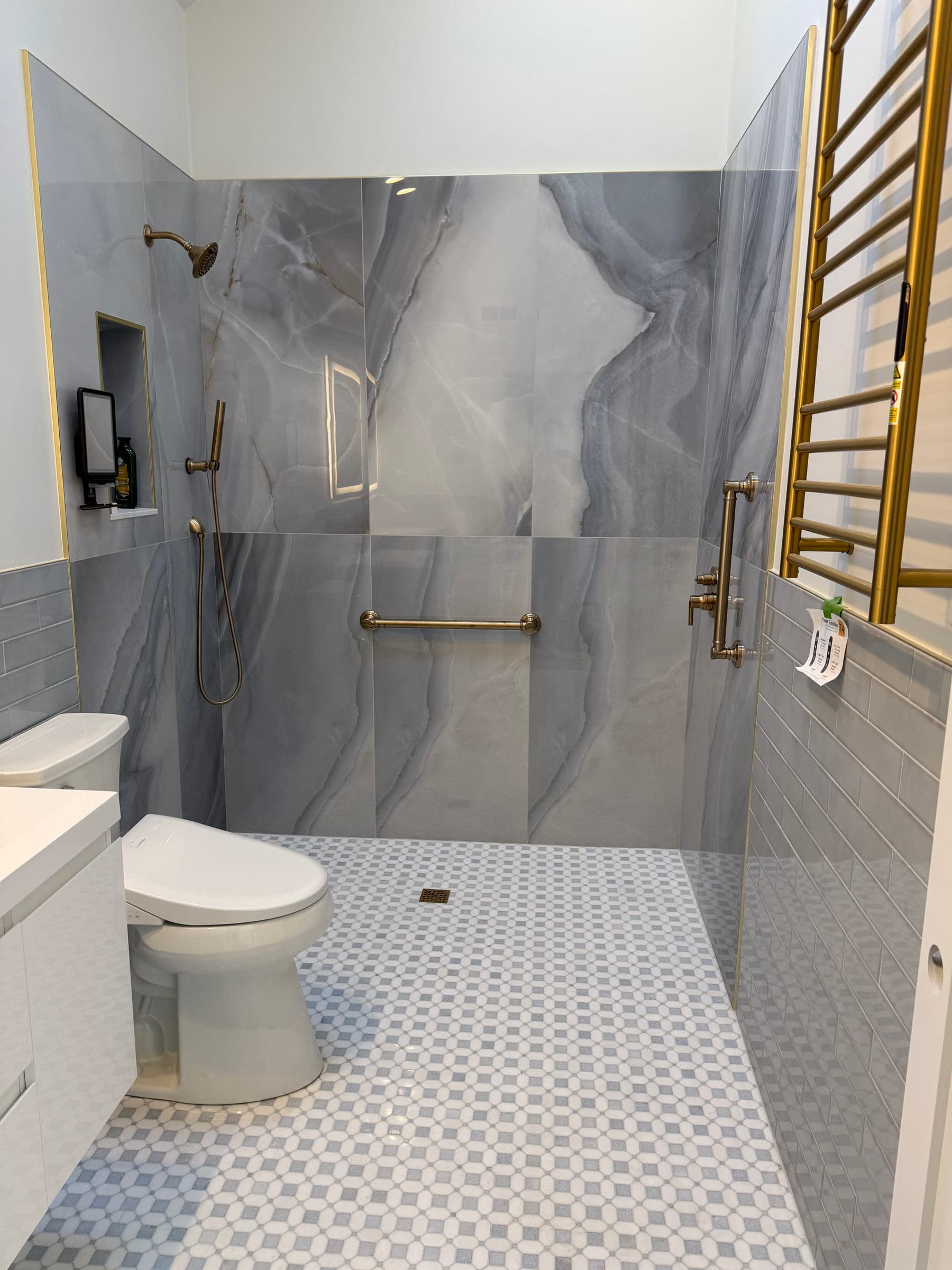 Level-access shower tiled in large-format stone-effect panels, with brass fittings, a grab rail and a heated towel rail