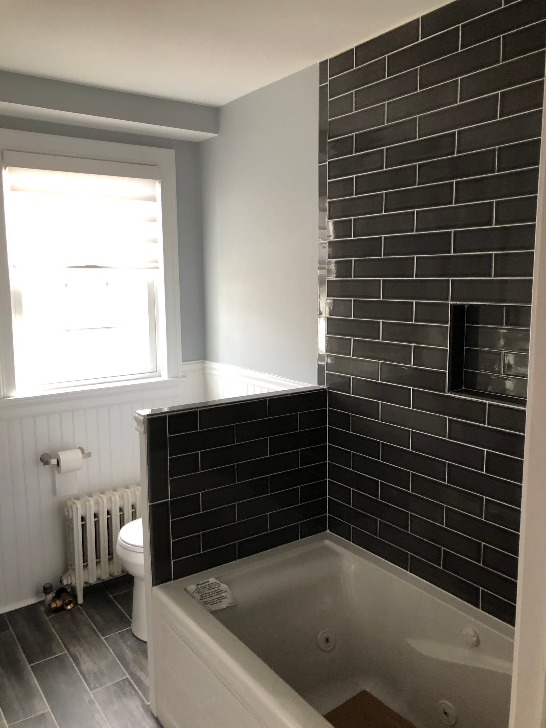 Finished bathroom with a dark subway tiled bath surround, white beadboard, a cast-iron radiator and wood-effect tile flooring
