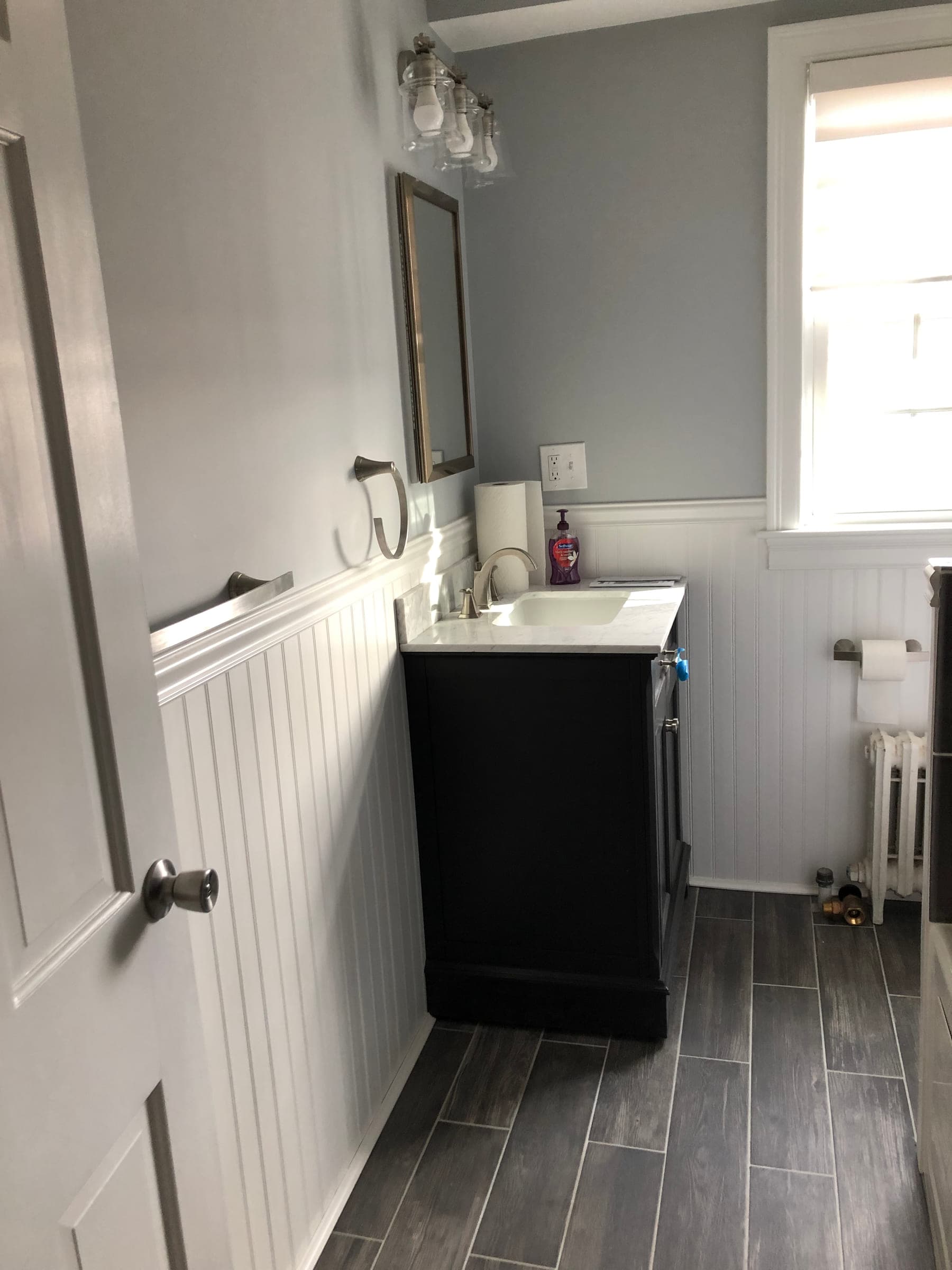 Bathroom vanity in dark timber against a white beadboard wall, with a framed mirror and a wall sconce