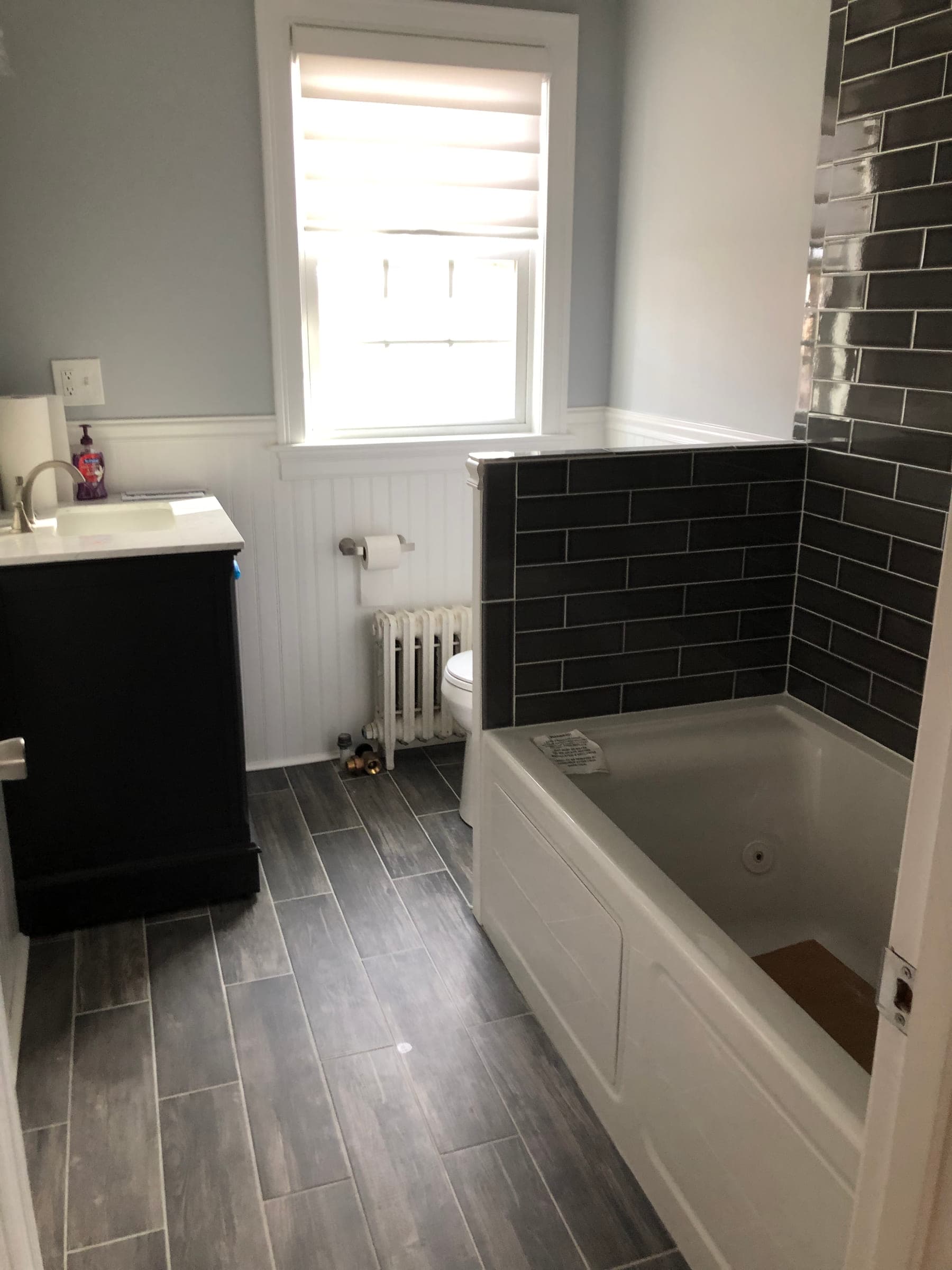 Finished bathroom with a dark tiled bath surround, wood-effect plank tile floor, beadboard wainscot and a dark vanity