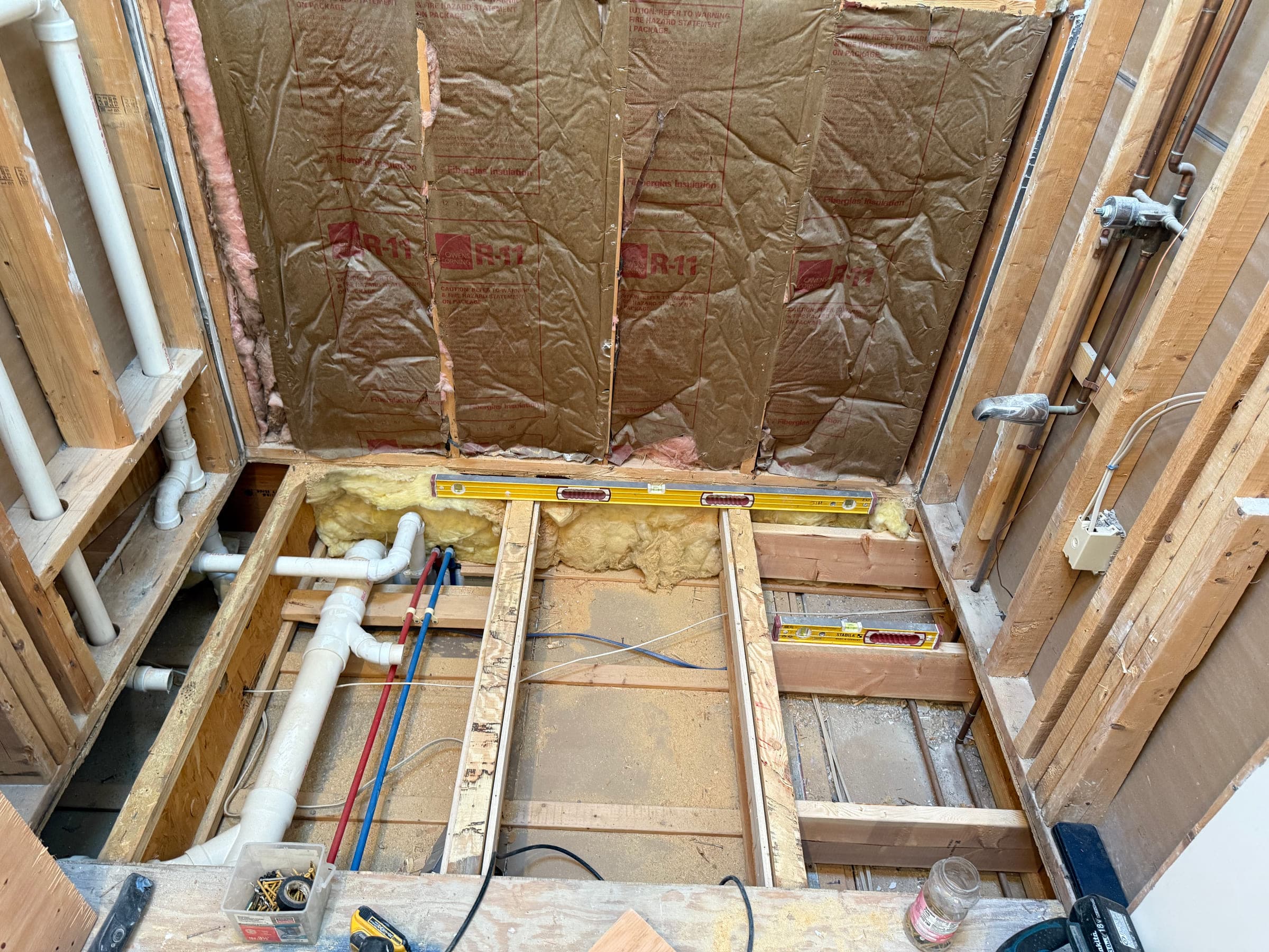 Bathroom floor opened up to the joists, with new hot and cold runs and a waste pipe installed and a level laid across the joists