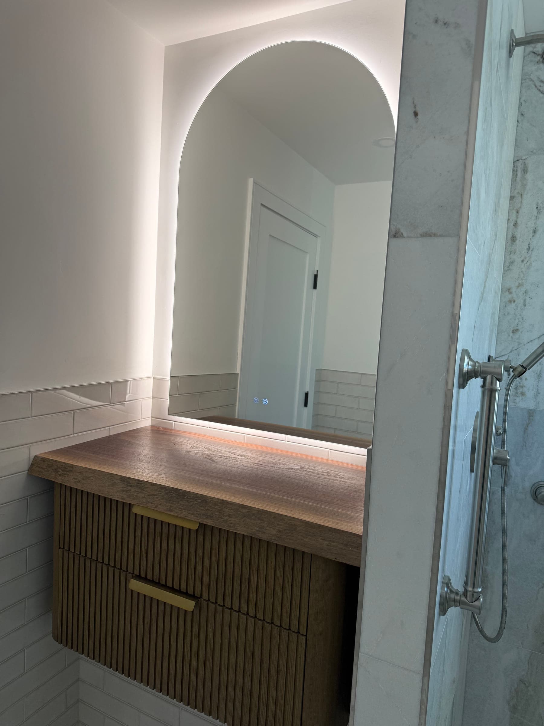 Floating fluted timber vanity with a thick timber top and a backlit arched mirror above