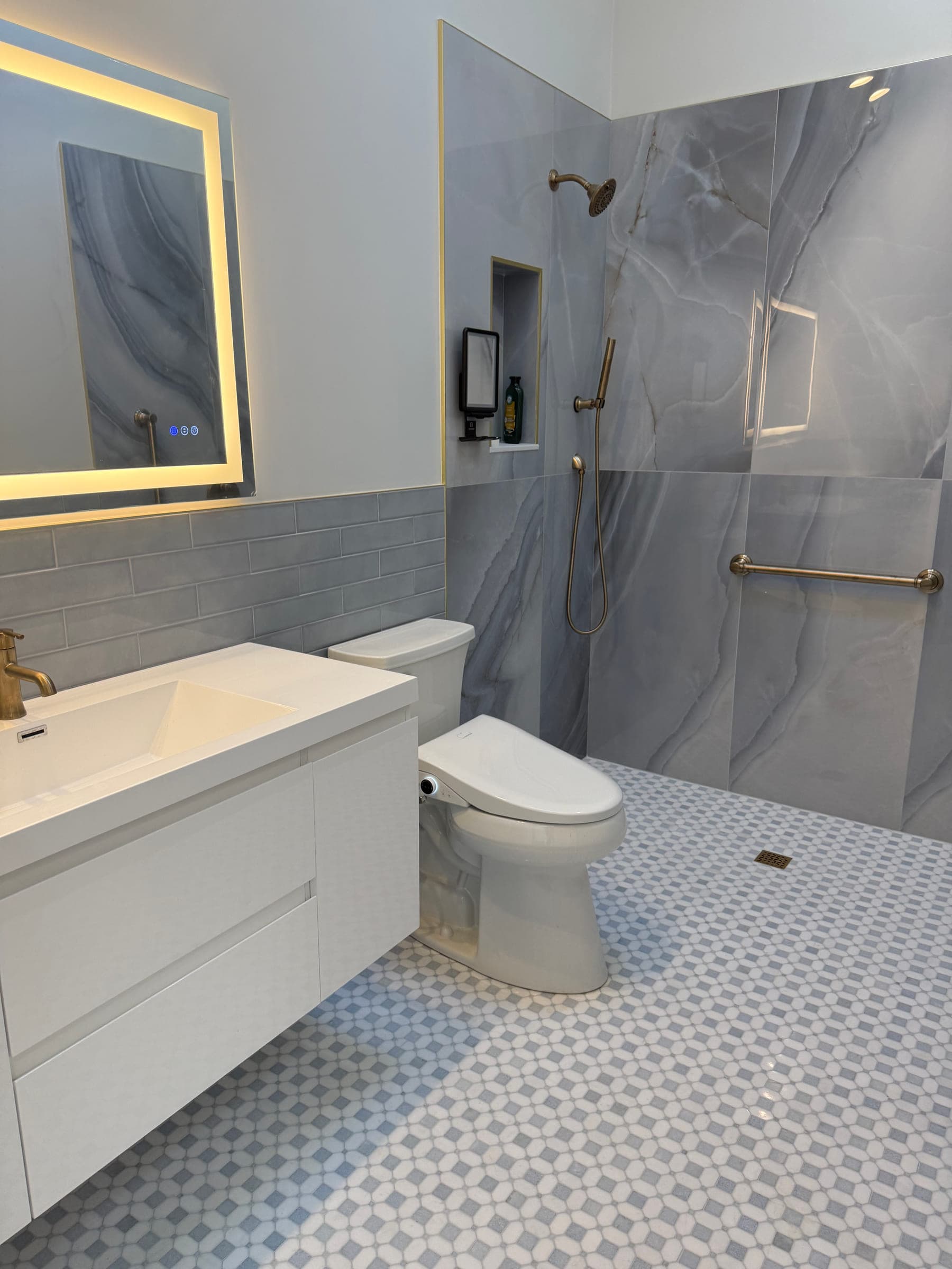 Finished bathroom with a grey stone-effect tiled walk-in shower, floating white vanity and backlit mirror