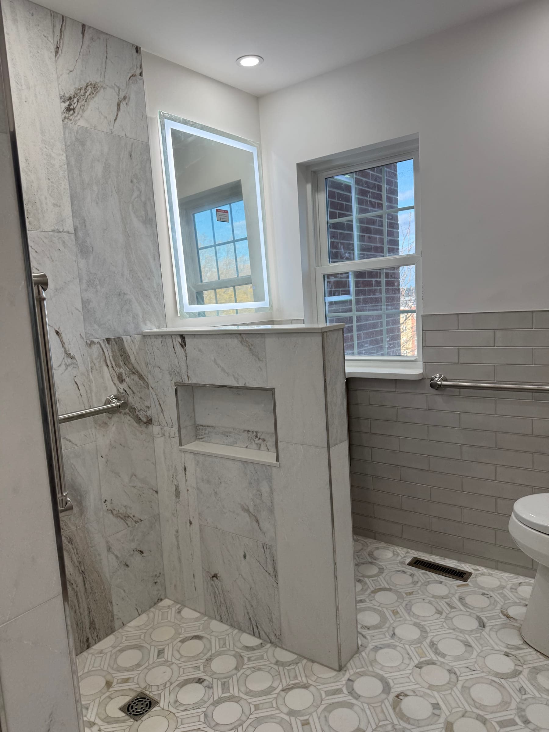 Tiled knee wall with a recessed niche and a stone cap, beside a window and a backlit mirror
