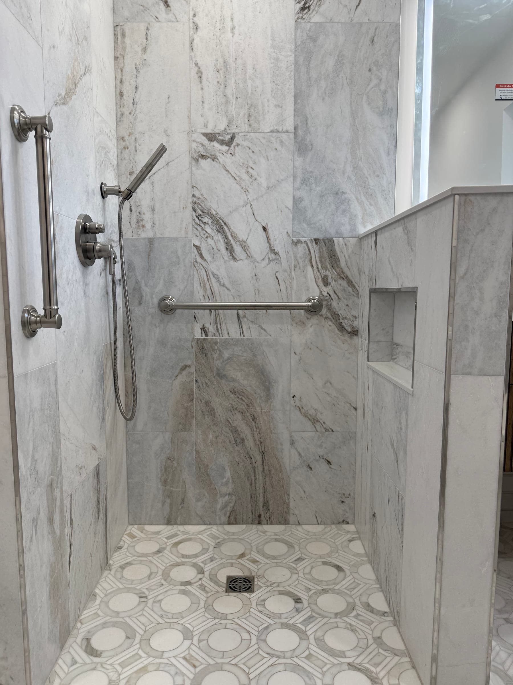 Curbless shower tiled in large-format marble-effect tile, with a recessed niche and two grab rails