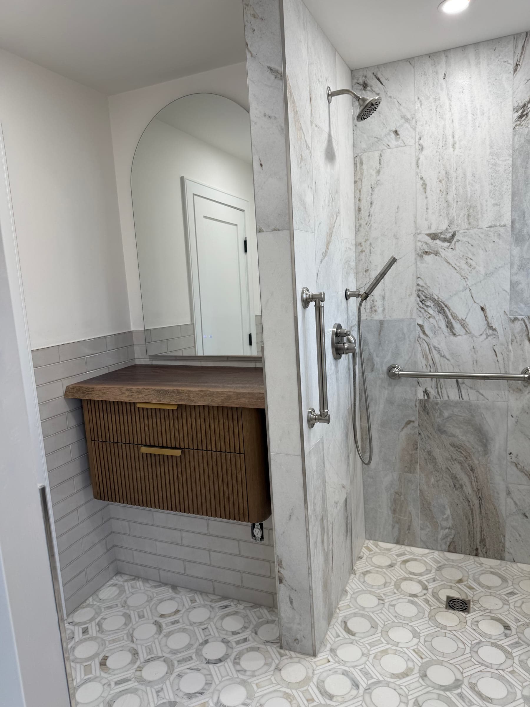 Finished bathroom with a marble-effect tiled walk-in shower, floating fluted vanity and patterned mosaic floor