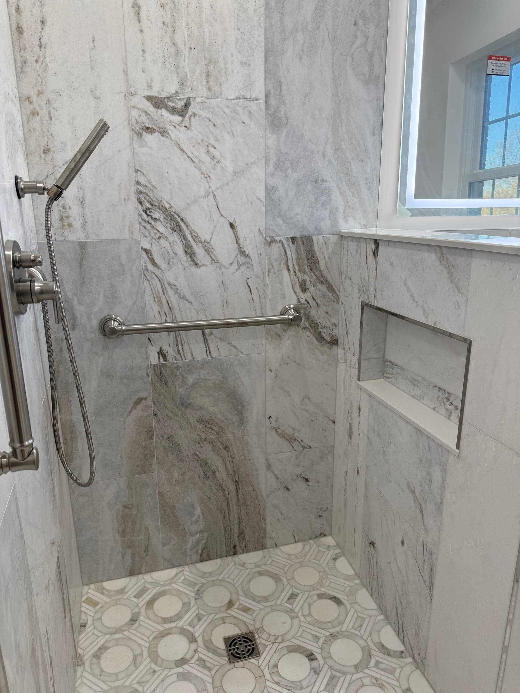 Recessed shower niche with mitred tile edges, set into a marble-effect tiled wall beside a grab rail