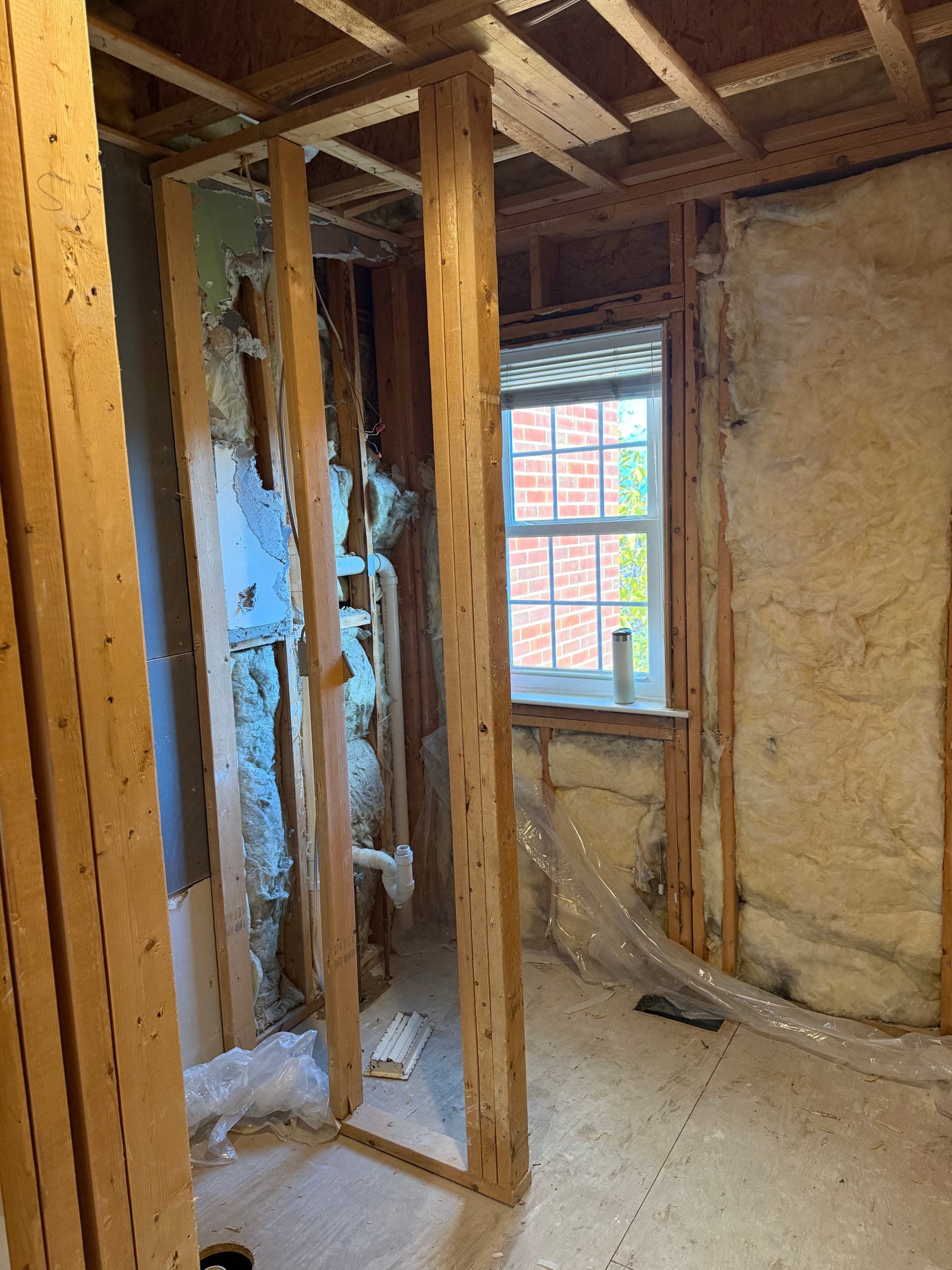 Bathroom opened up to the studs, showing insulation, exposed plumbing and a window opening
