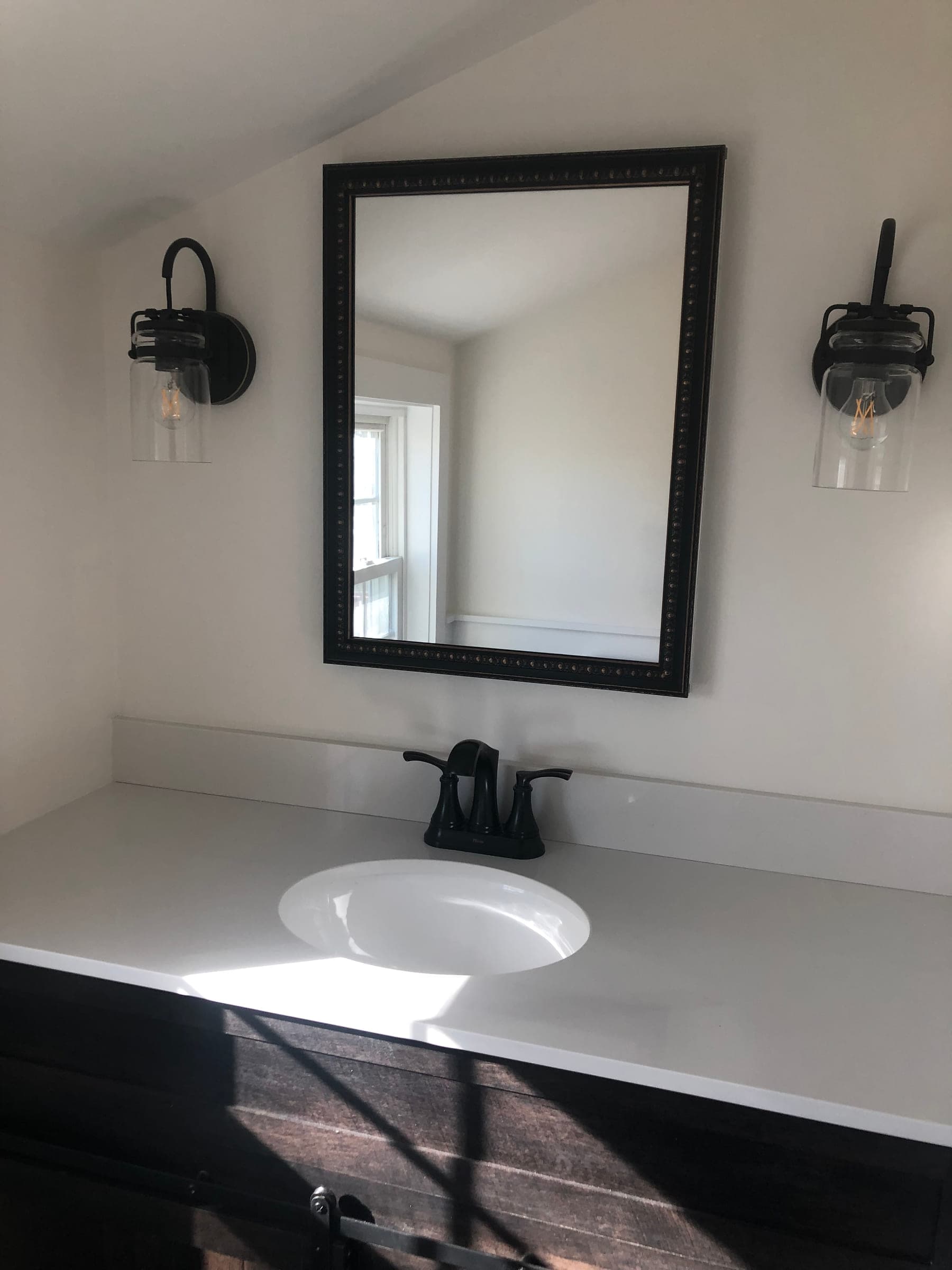 Bathroom vanity with a white stone top, an undermount basin, a black framed mirror and a pair of black glass sconces