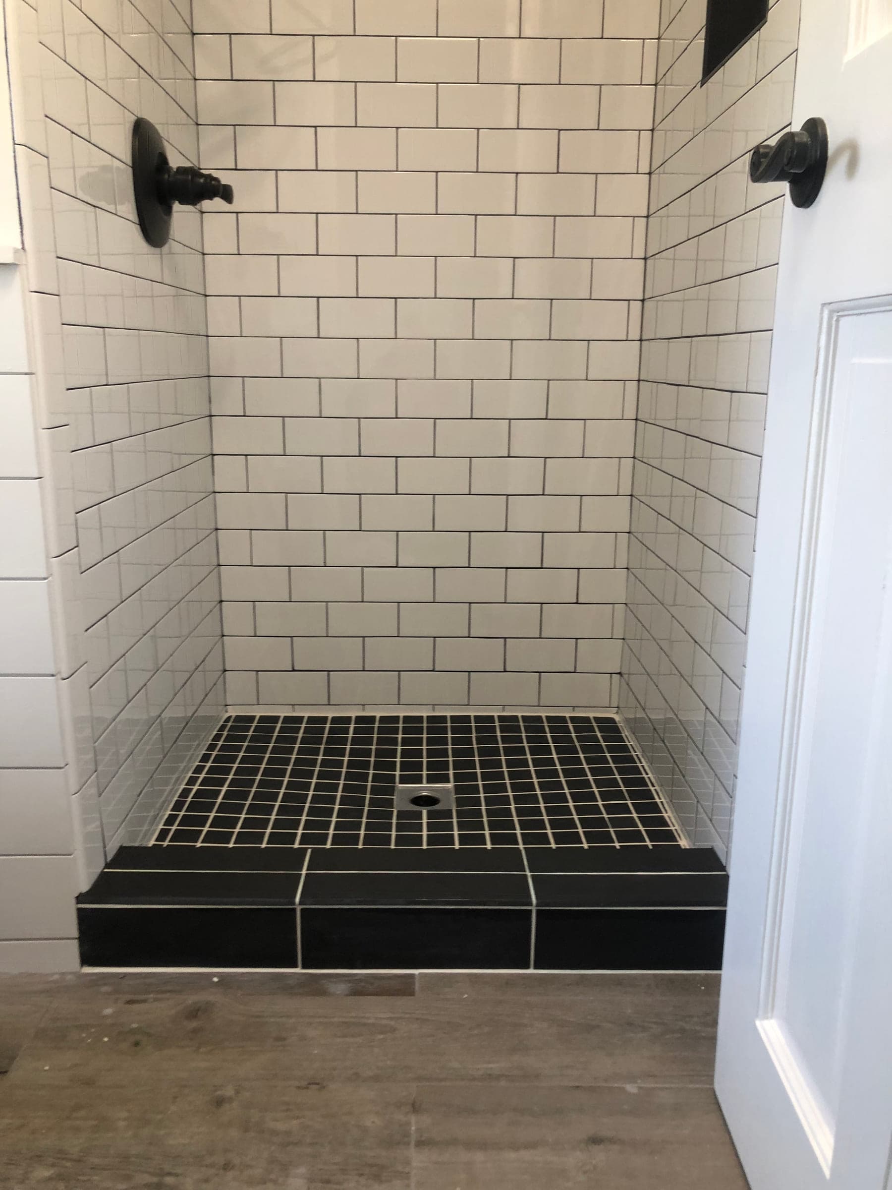 Shower tiled in white subway tile with a black mosaic floor, a tiled curb and matte black fittings
