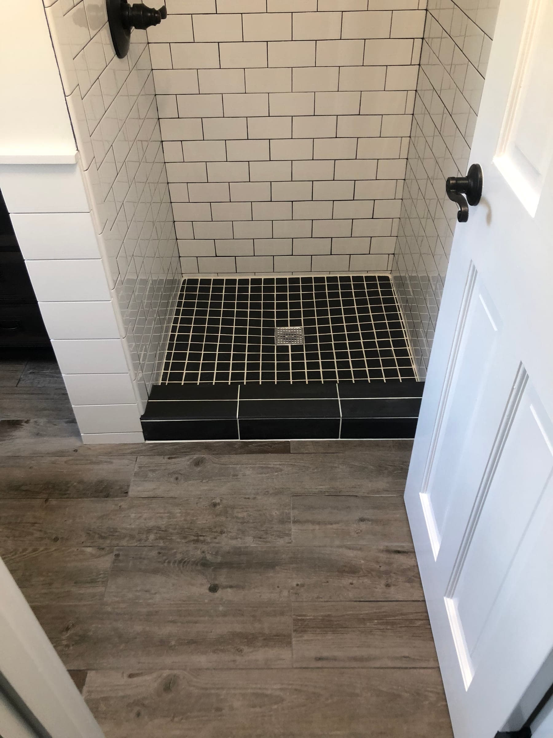 White subway tiled shower with a black mosaic floor and curb, opening onto wood-effect plank flooring