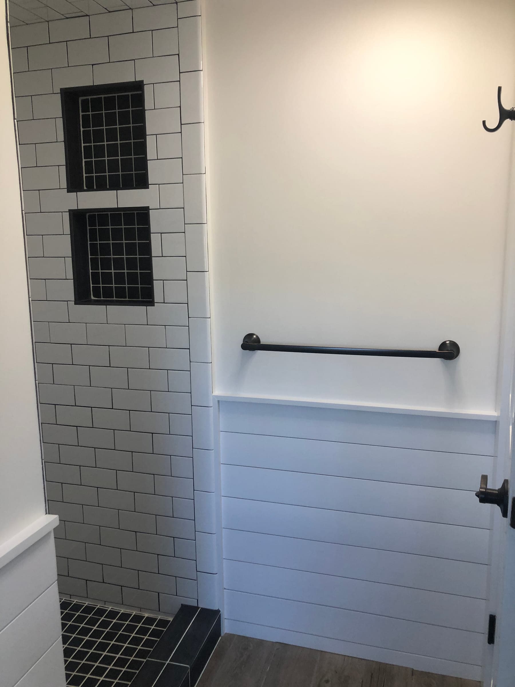 White subway tiled bath surround with two recessed black niches, a matte black grab rail and a shiplap half wall