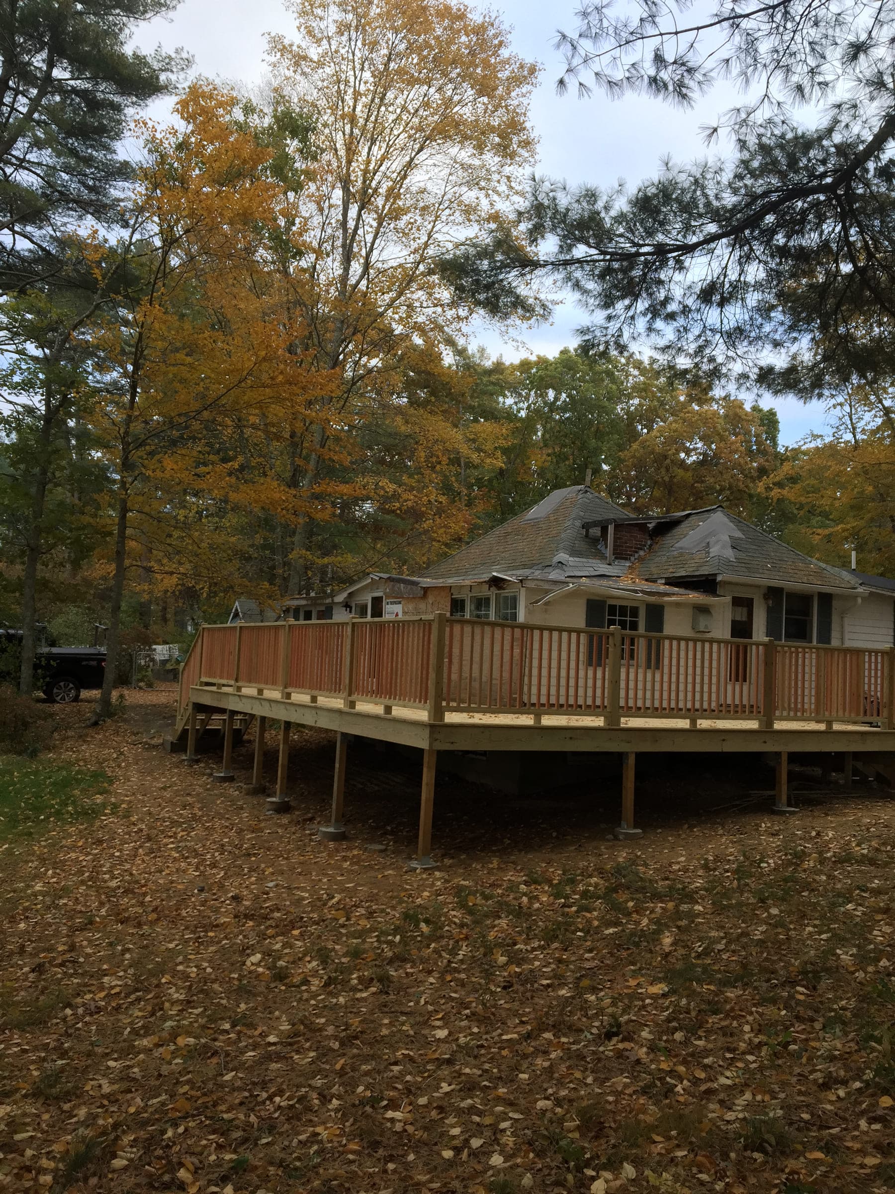 A large new deck framed on footings and wrapping around a house, with the roof stripped back for renovation