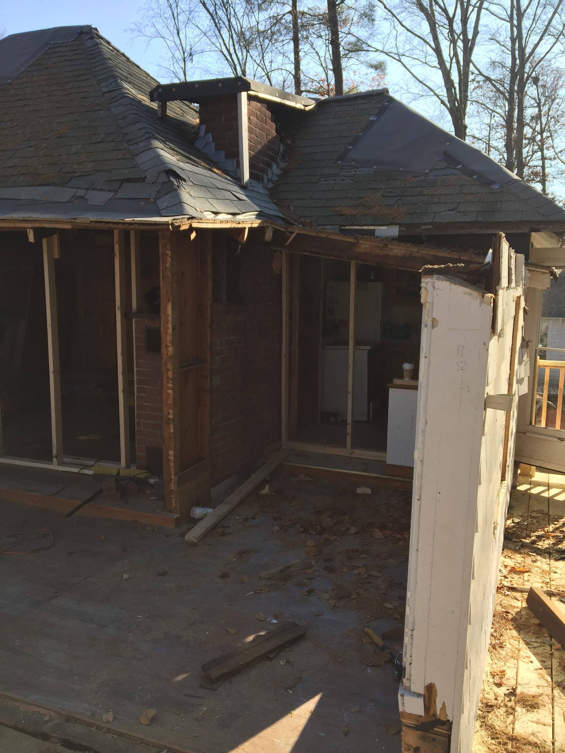 A porch stripped back to the studs with the siding removed, exposing the brick chimney and roof structure