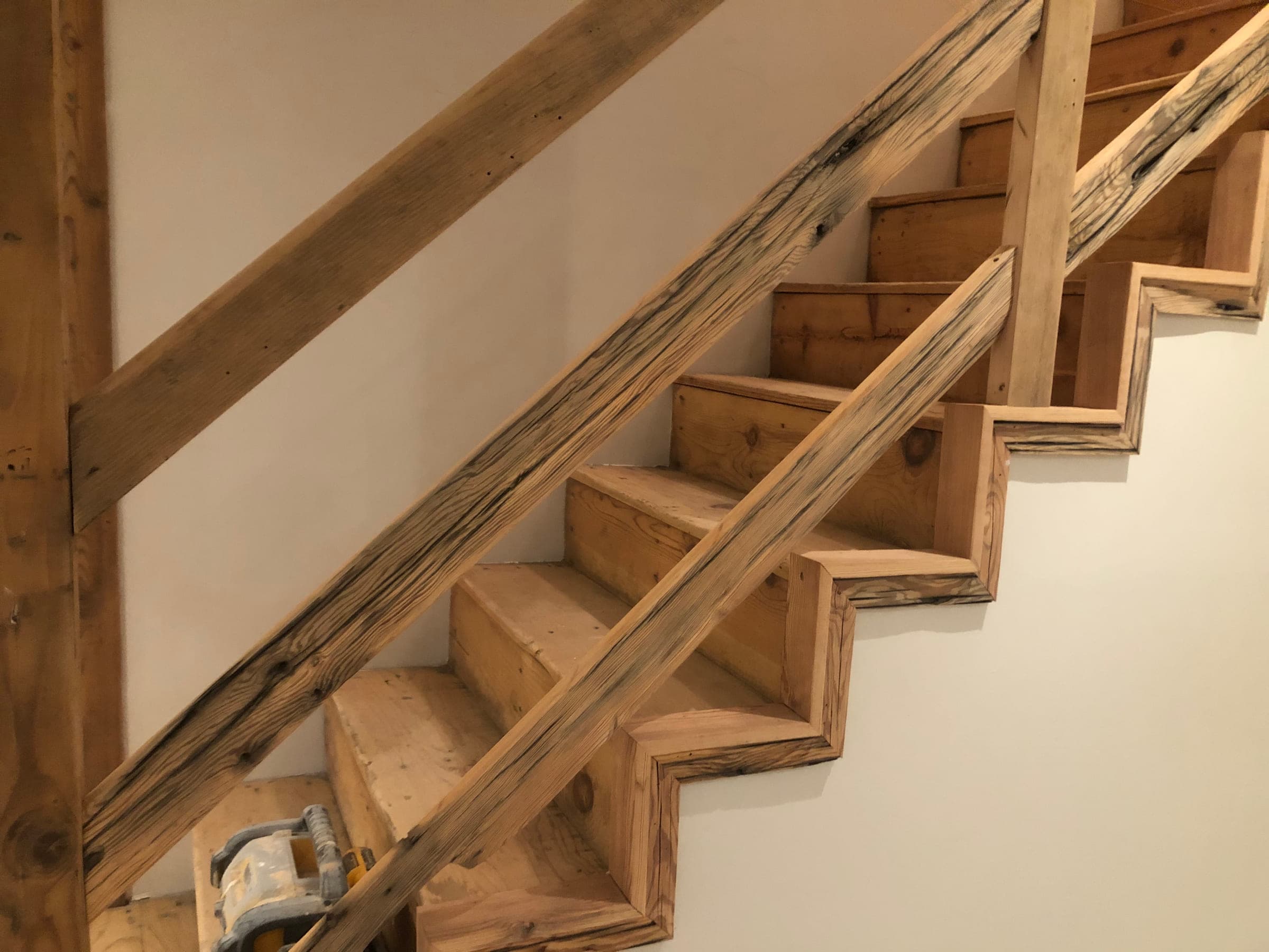 Close-up of a reclaimed timber staircase with open risers and a rough-sawn handrail