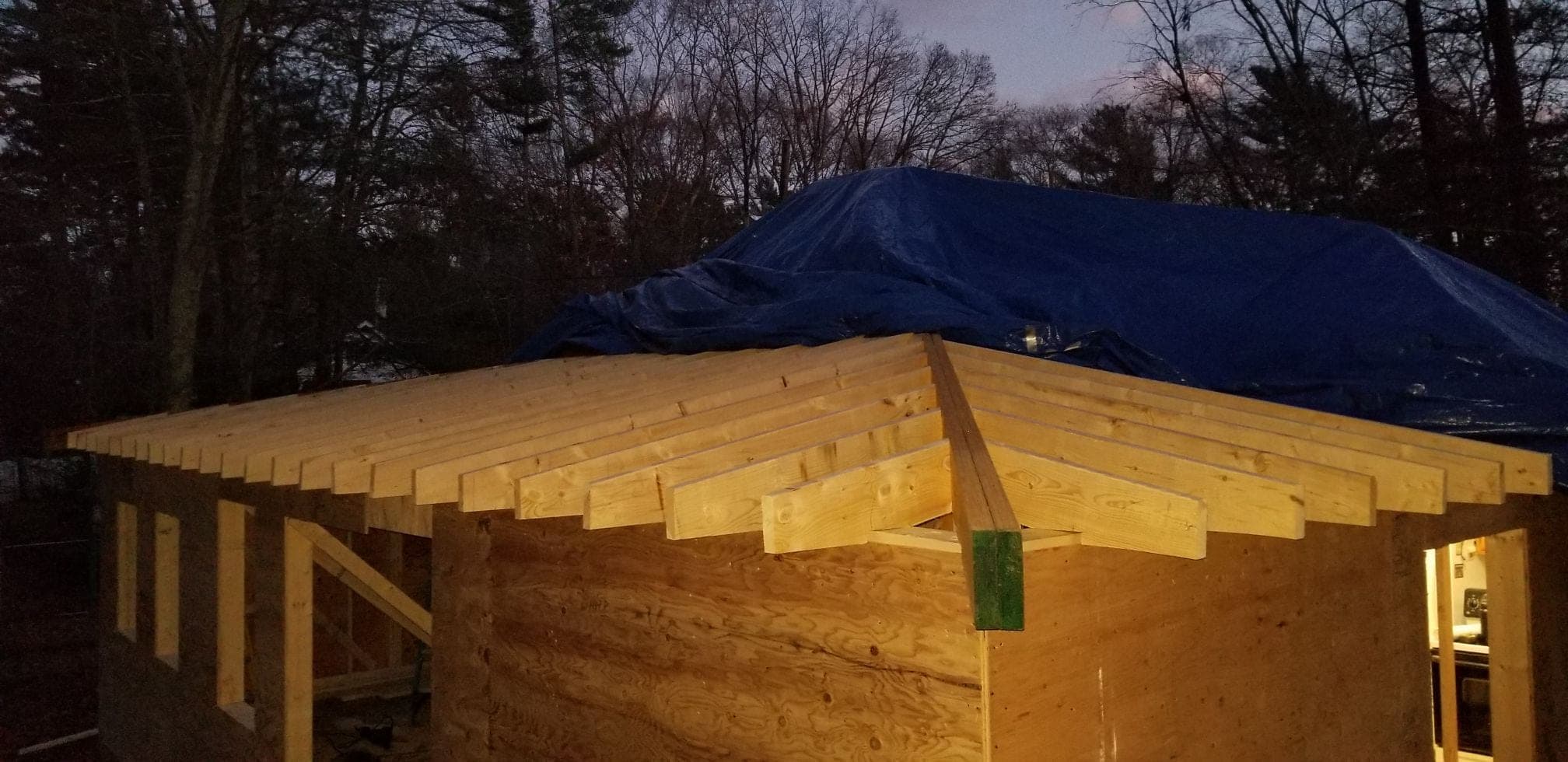 Hip roof framing at dusk, with rafter tails projecting over sheathed walls