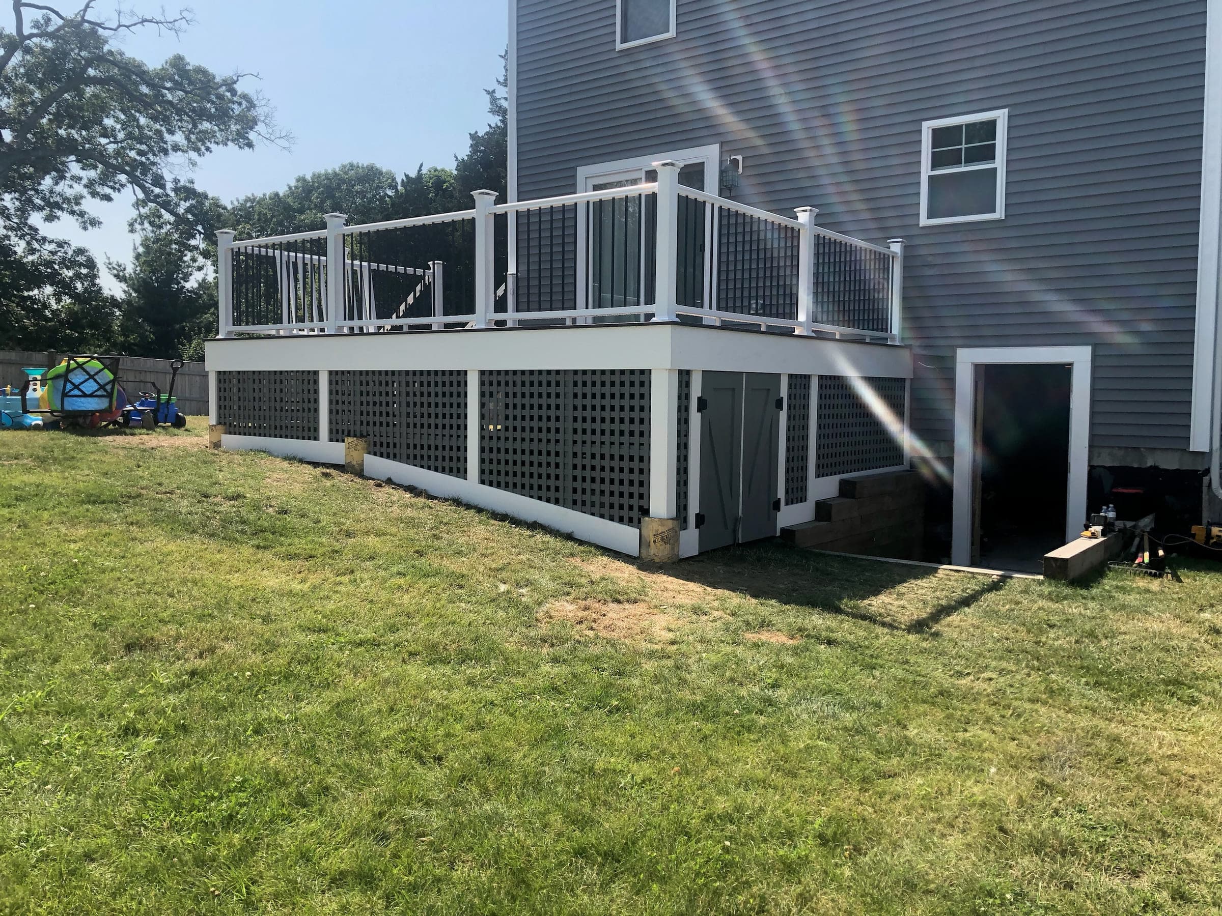 Finished raised deck with white railings, metal balusters and a lattice skirt with an access door below