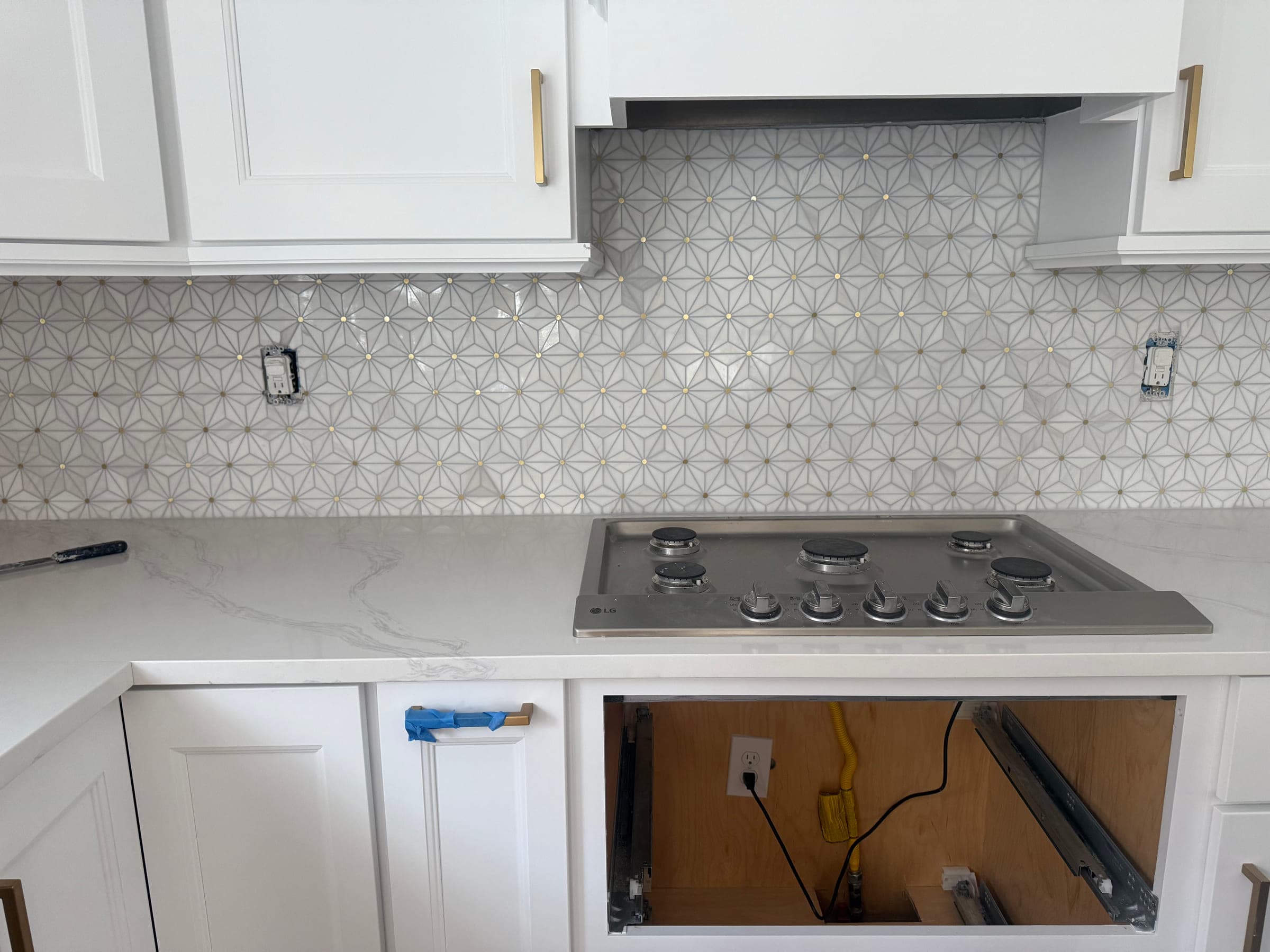 Stainless cooktop in a quartz worktop beneath a patterned star-tile splashback and a beadboard range hood