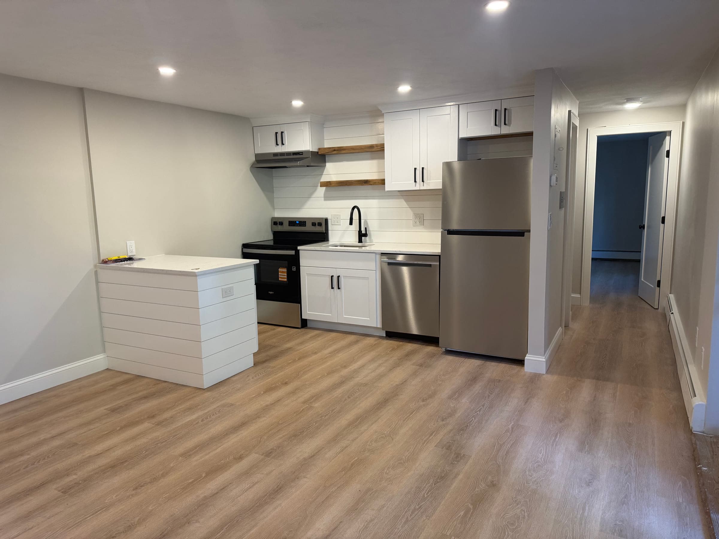 Open-plan kitchen and living space with wood-effect flooring, looking through to a hallway