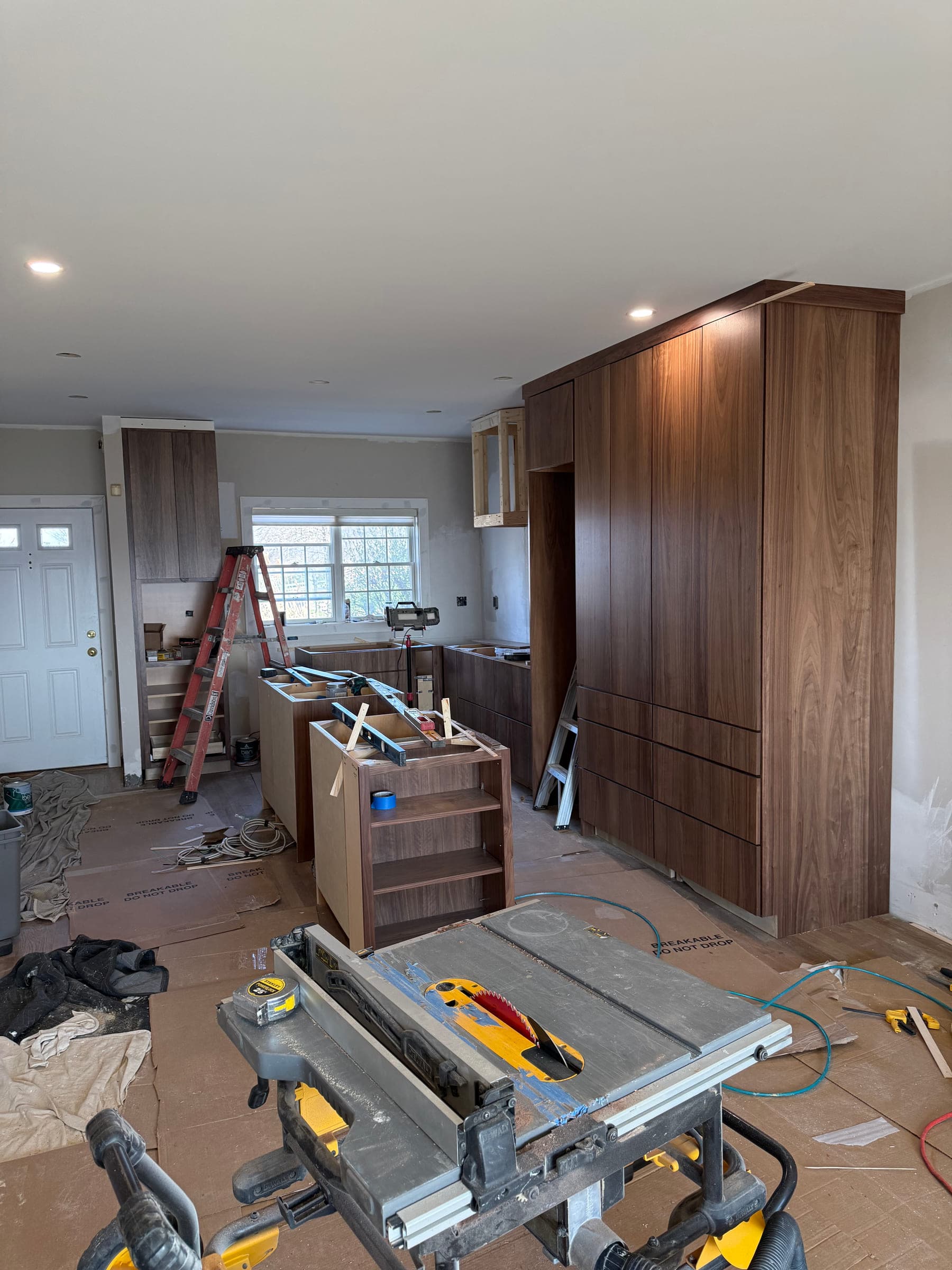 Kitchen installation in progress with walnut cabinetry, a table saw and protective covering over the floor