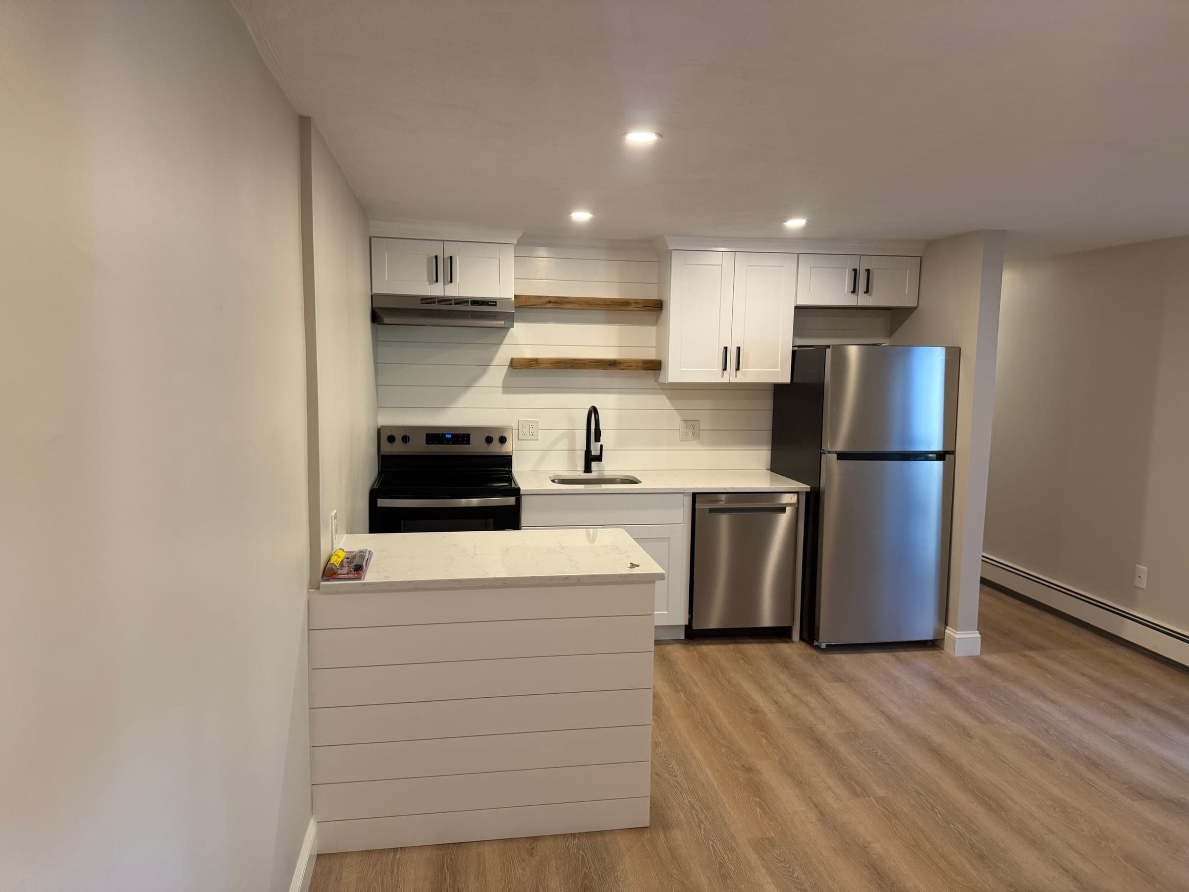 Kitchen peninsula clad in shiplap with a quartz top, beside a run of white cabinets and stainless appliances