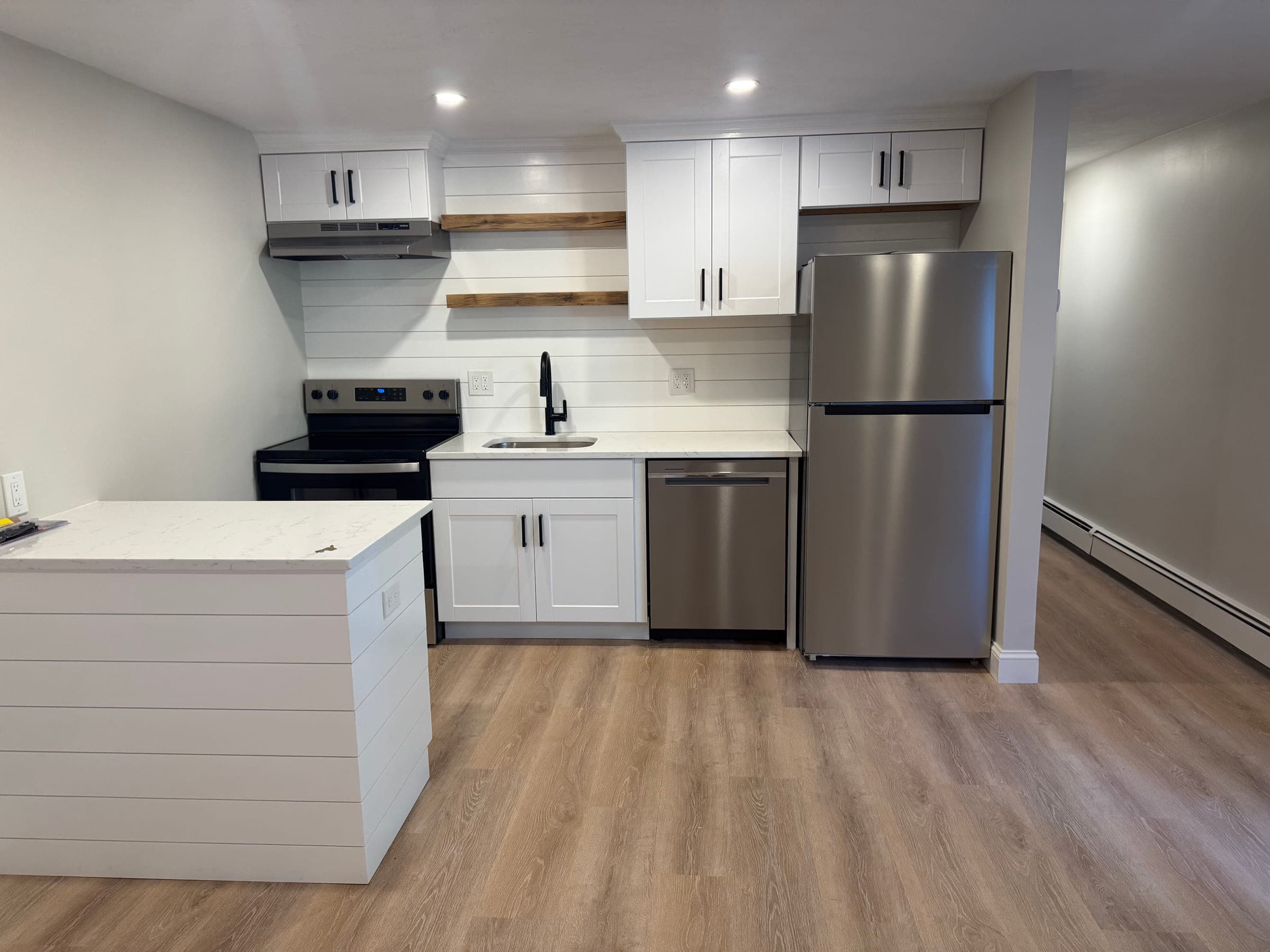 Finished kitchen with white shaker cabinets, quartz worktops, a shiplap splashback and open timber shelves