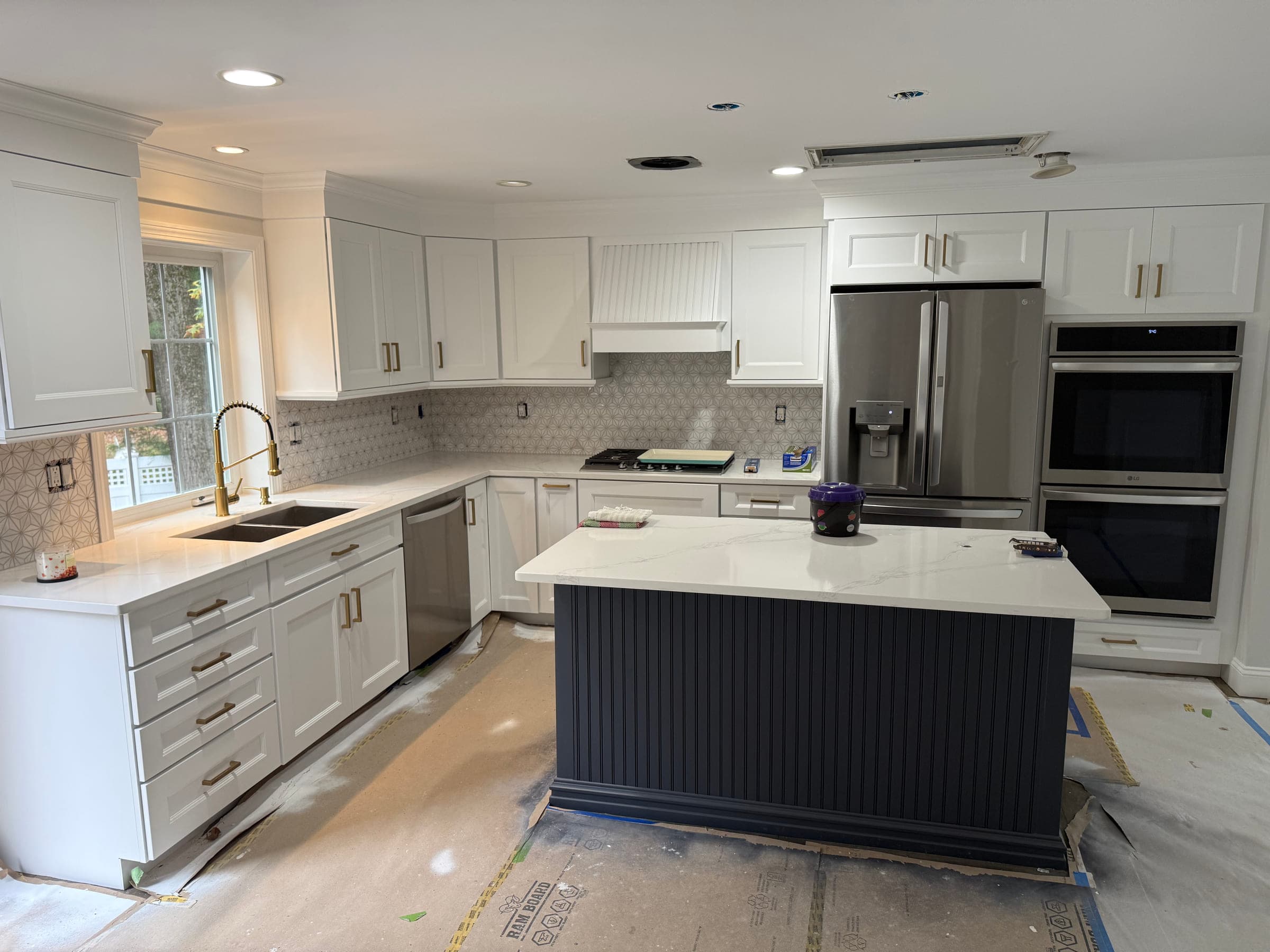 Finished kitchen with white shaker cabinets, quartz worktops, a dark fluted island, stainless double ovens and a patterned tile splashback