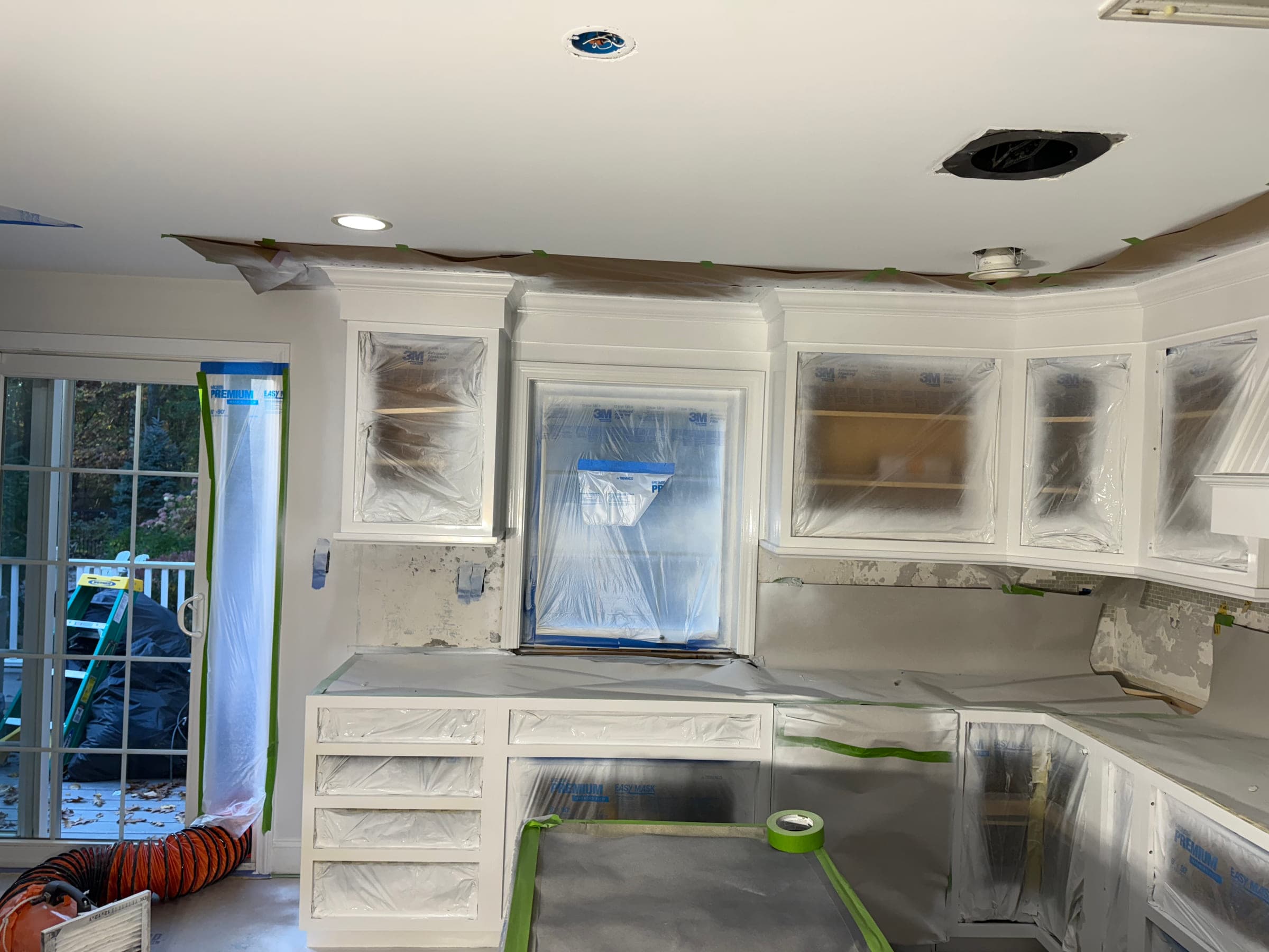 A kitchen fully masked for spraying, with cabinets wrapped in plastic, worktops covered, the ceiling line papered and tape along every edge