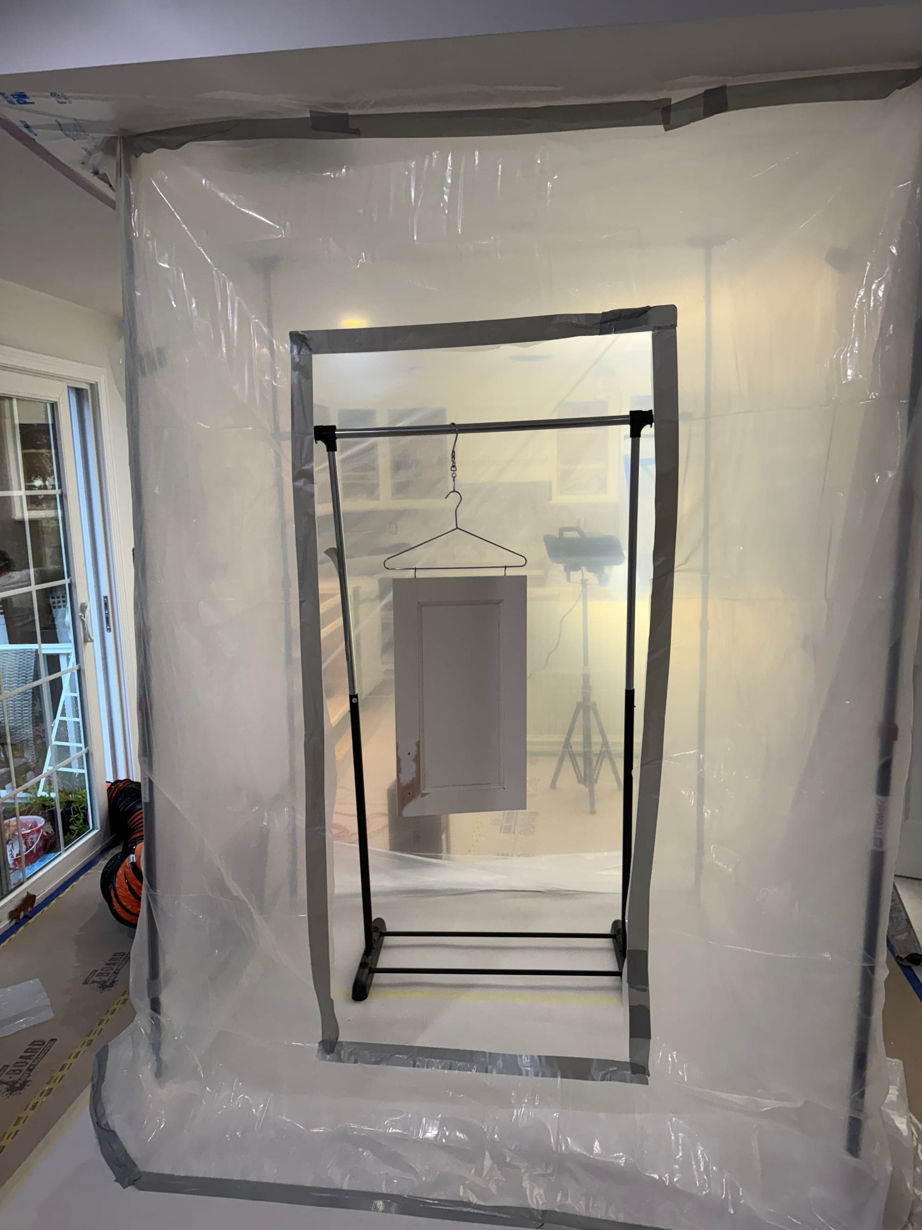 A sealed spray booth built on site from plastic sheeting, taped floor to ceiling, with a drying rack inside and the floor papered and taped