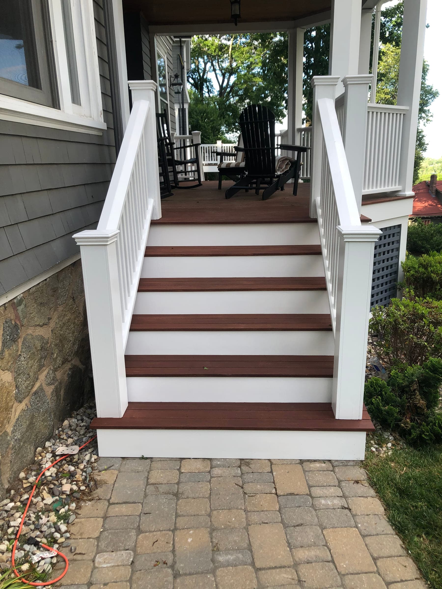 Rebuilt front porch steps seen head-on from the paved path, with hardwood treads, painted white risers and a painted balustrade either side