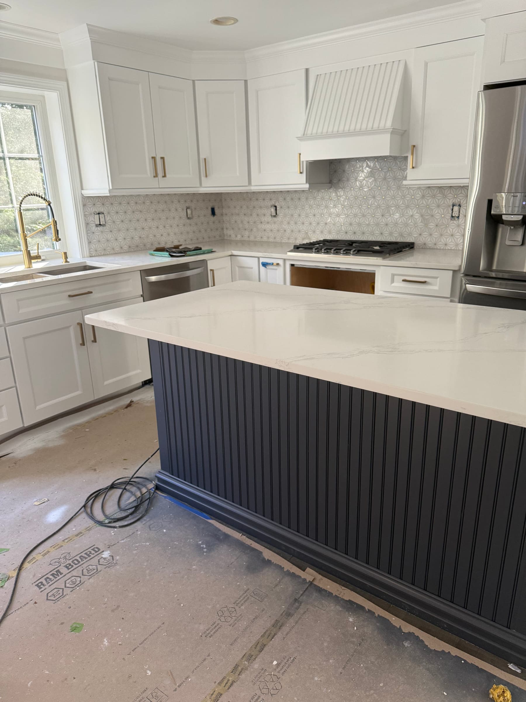 Dark fluted kitchen island with a quartz top, facing white shaker cabinets and a beadboard range hood
