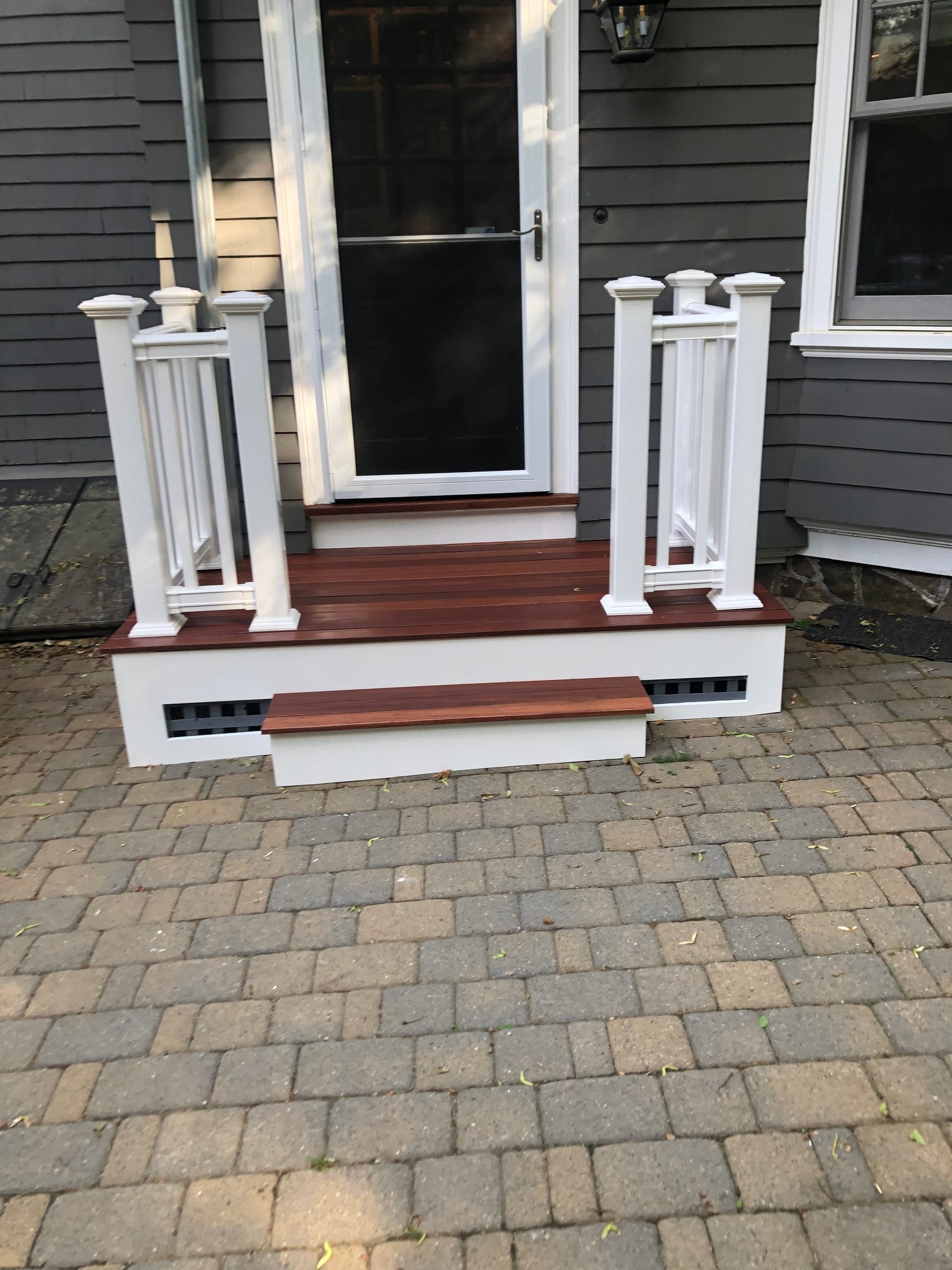 Top of the porch steps at the entrance, with a hardwood tread, two painted newel posts and a storm door