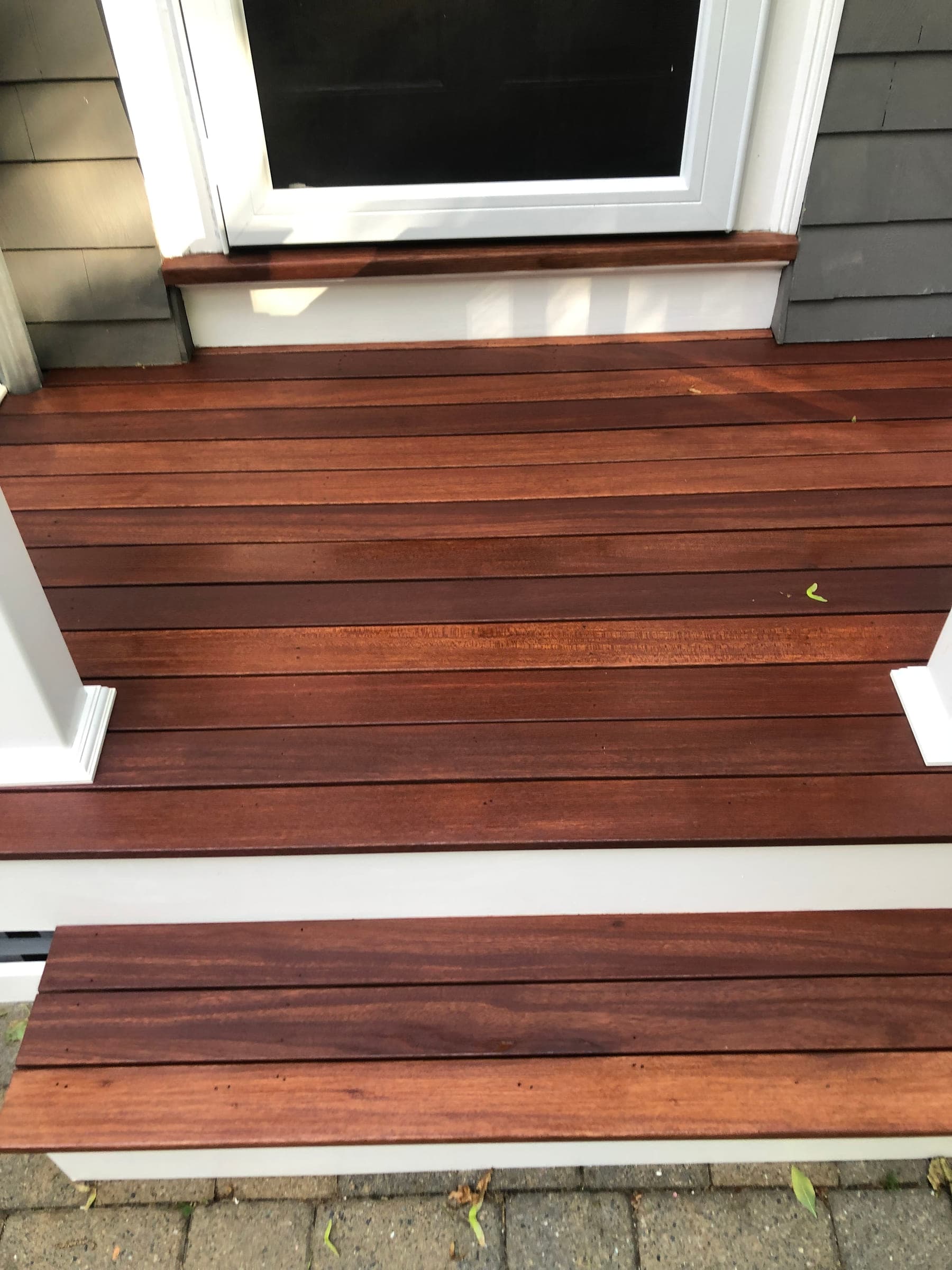 Close view of newly finished hardwood porch treads and the landing board, butted against white painted trim below a window