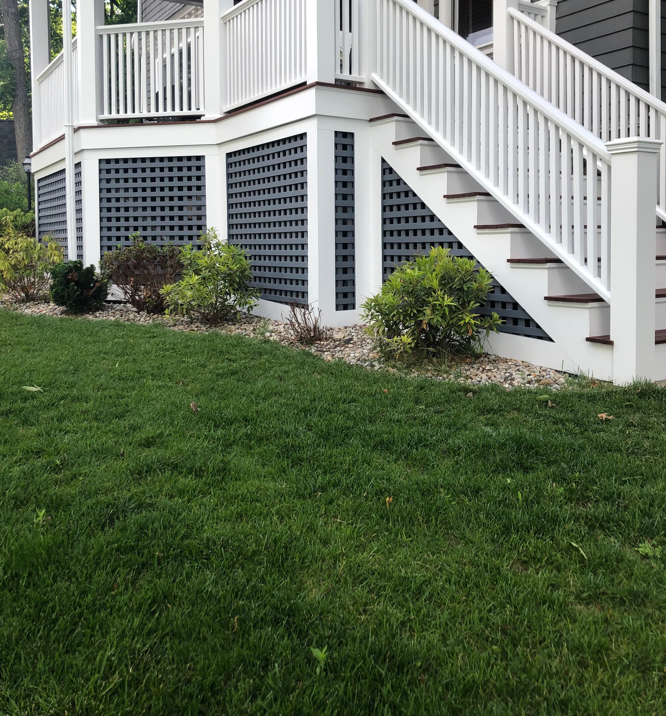 Side view of the porch showing the full run of painted railings and posts above dark lattice skirting